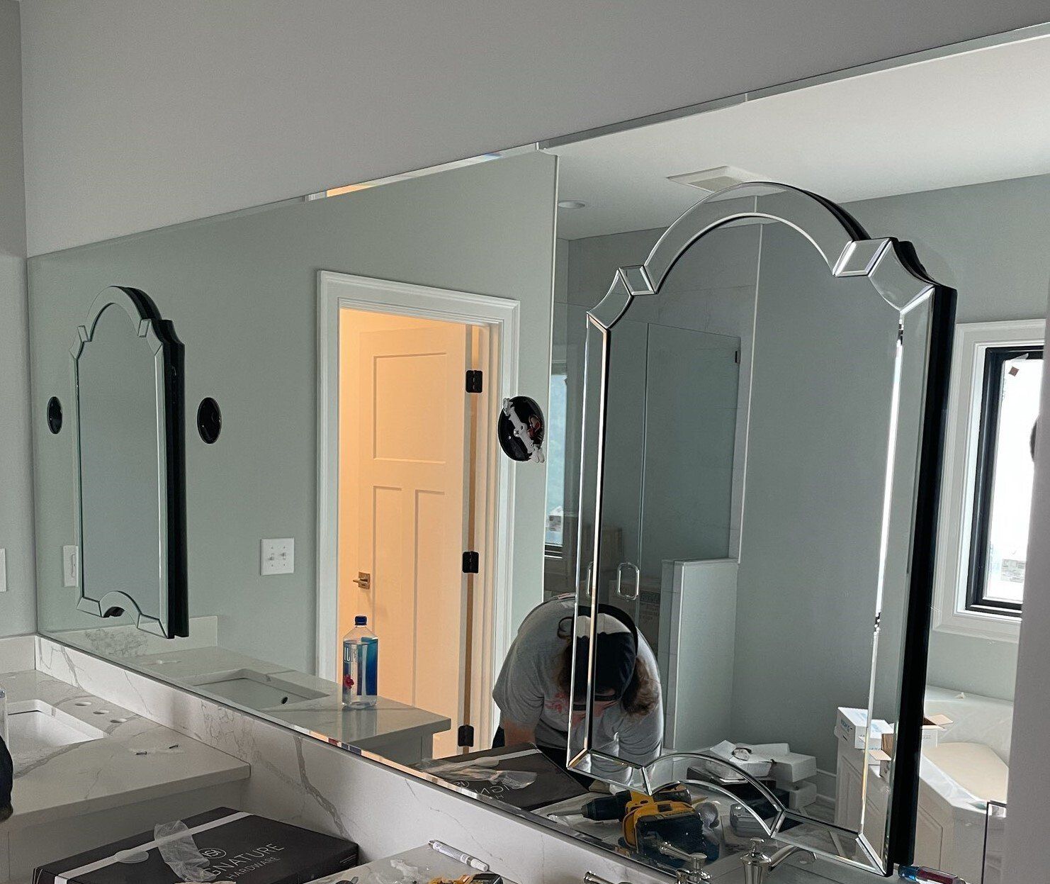 Bathroom mirrors being installed, including a decorative, arched mirror with an installer working.