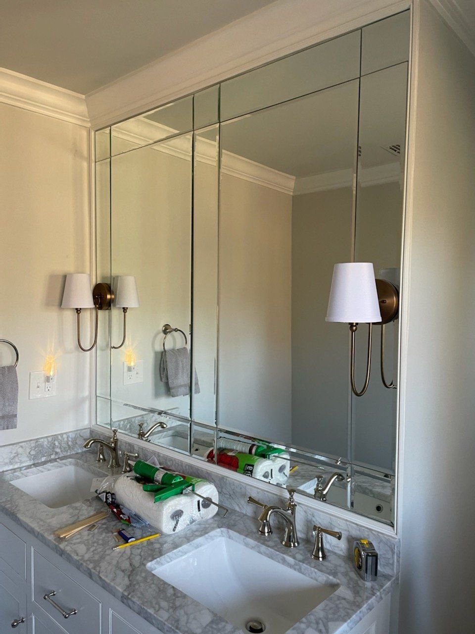 Bathroom with a large mirror, marble countertop, two sinks, and sconce lighting.