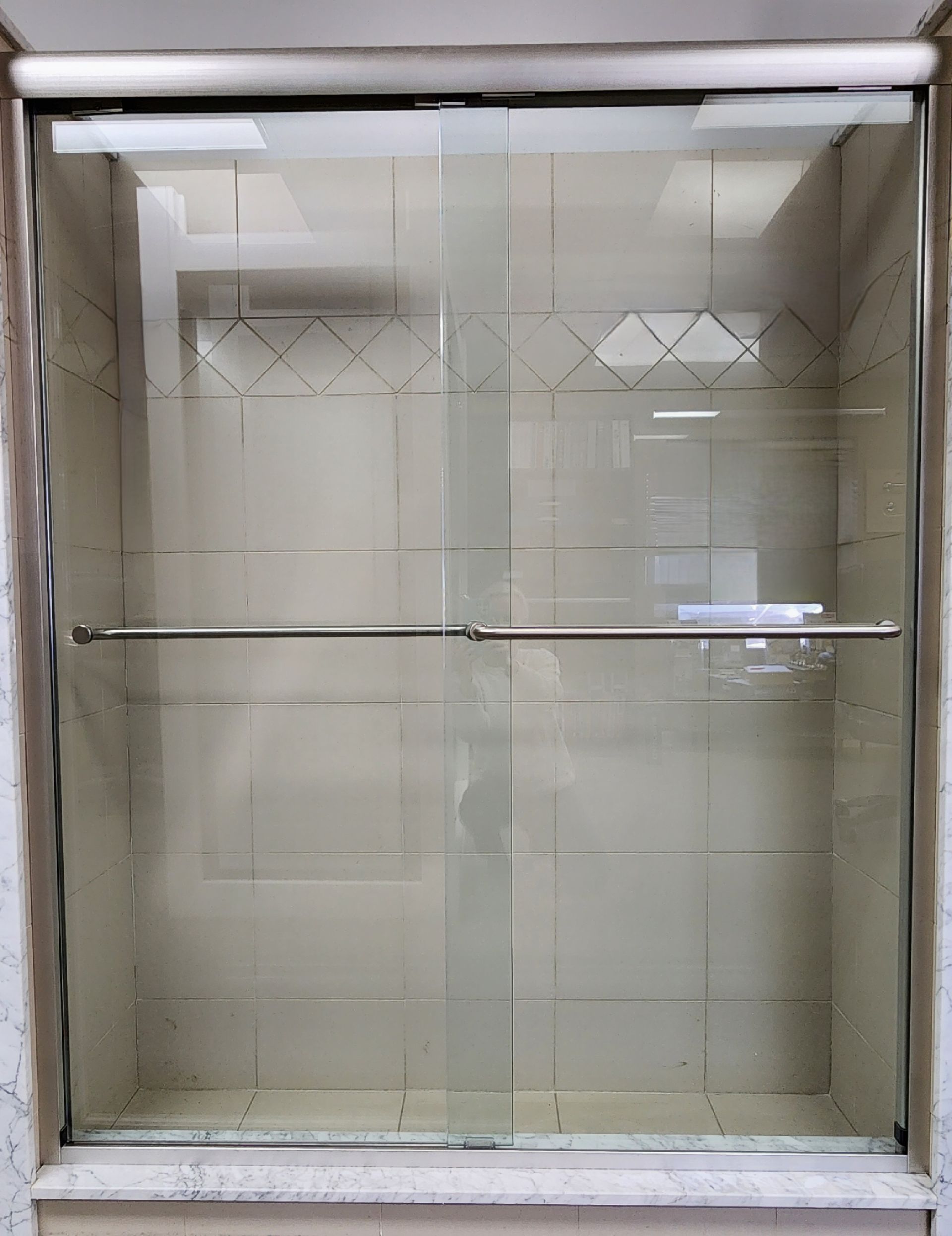 Glass shower enclosure with geometric etched design and a horizontal towel bar.