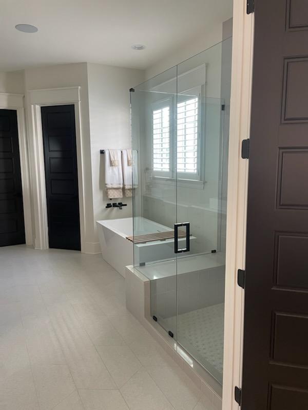 Modern bathroom with a glass shower, a white tub, and a window with shutters.