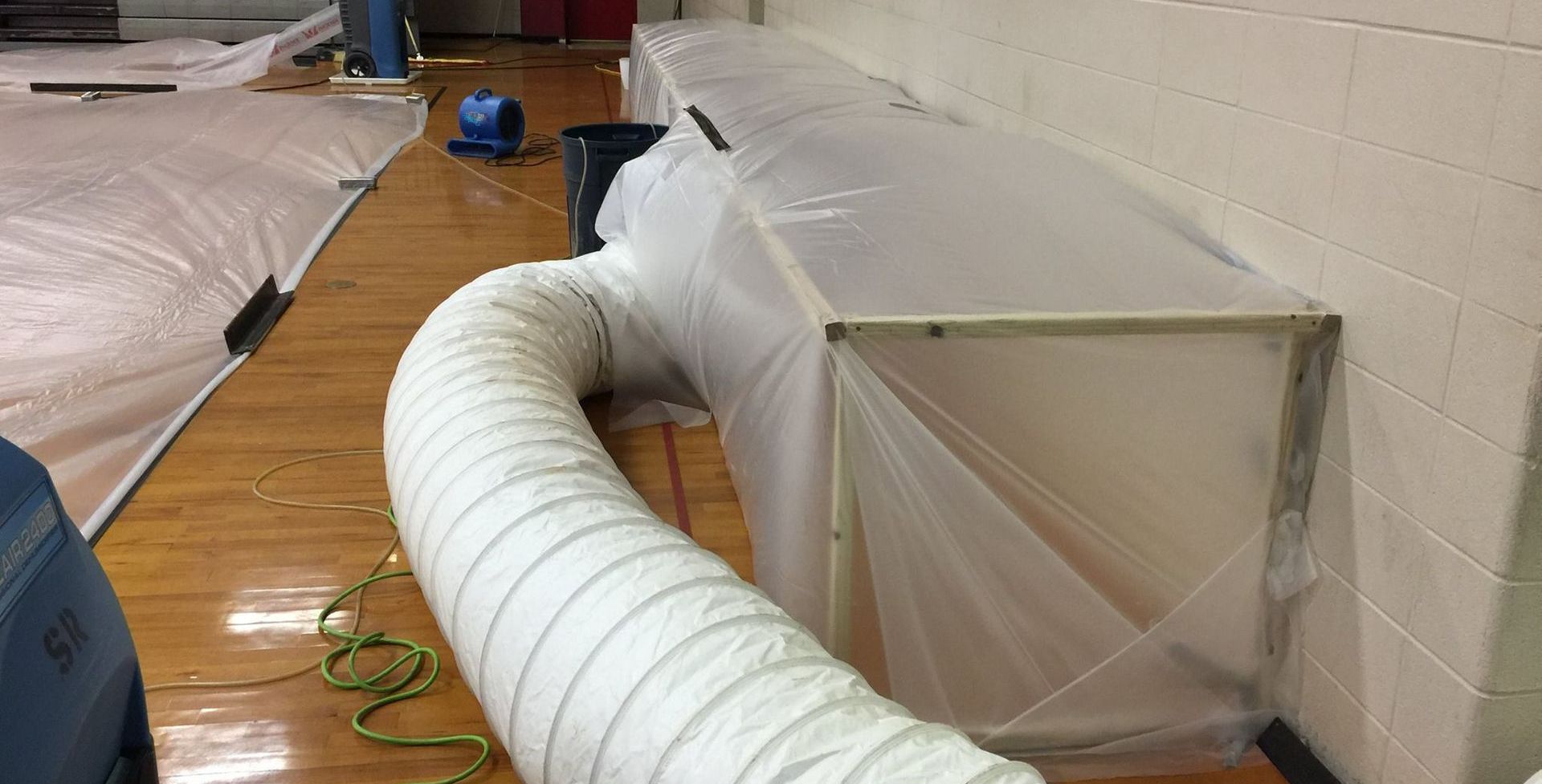 Containment setup in a gymnasium with plastic sheeting and a ventilation system.