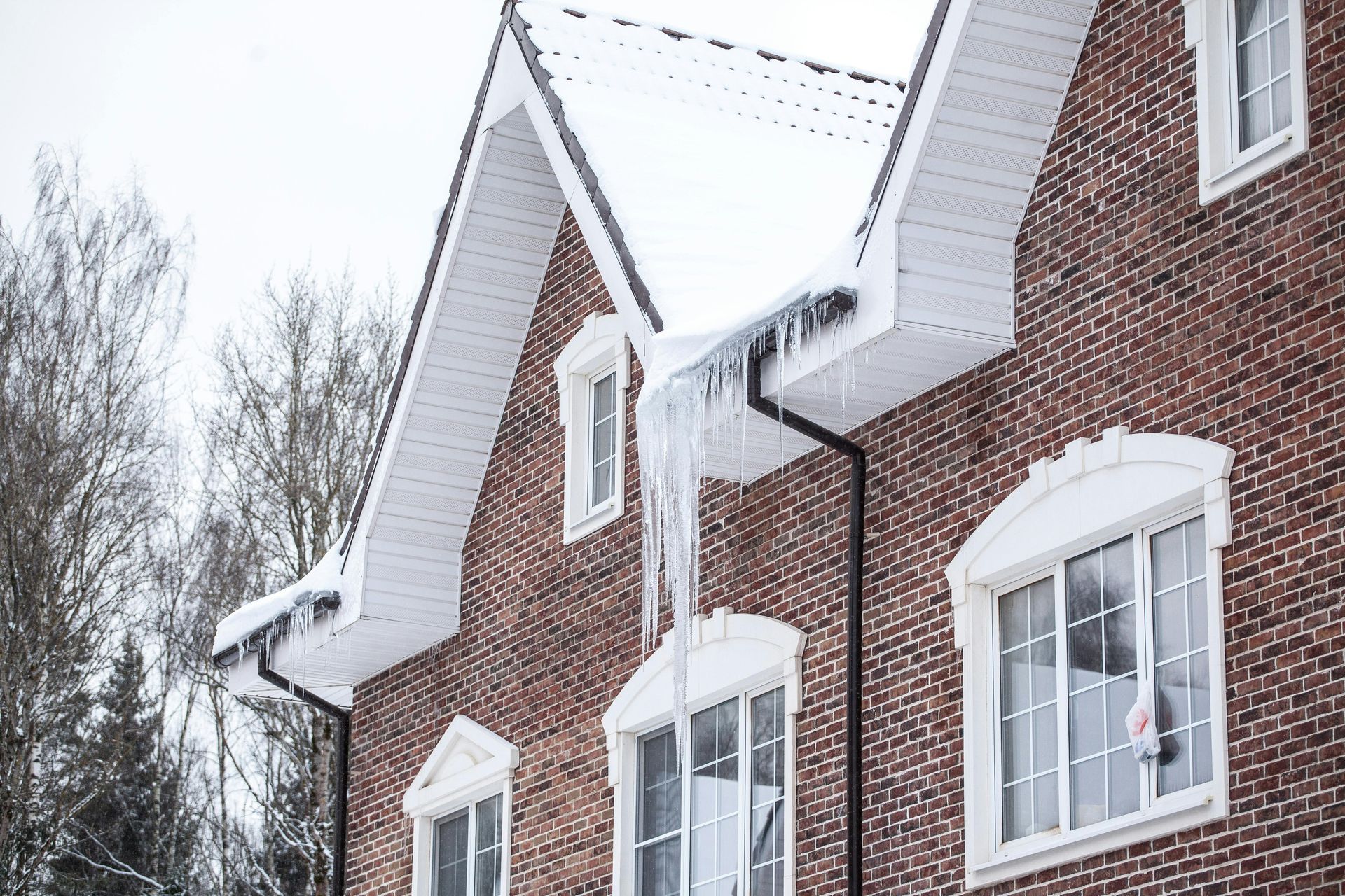 Brick house with icicles hanging from the roof and gutters, winter landscape.