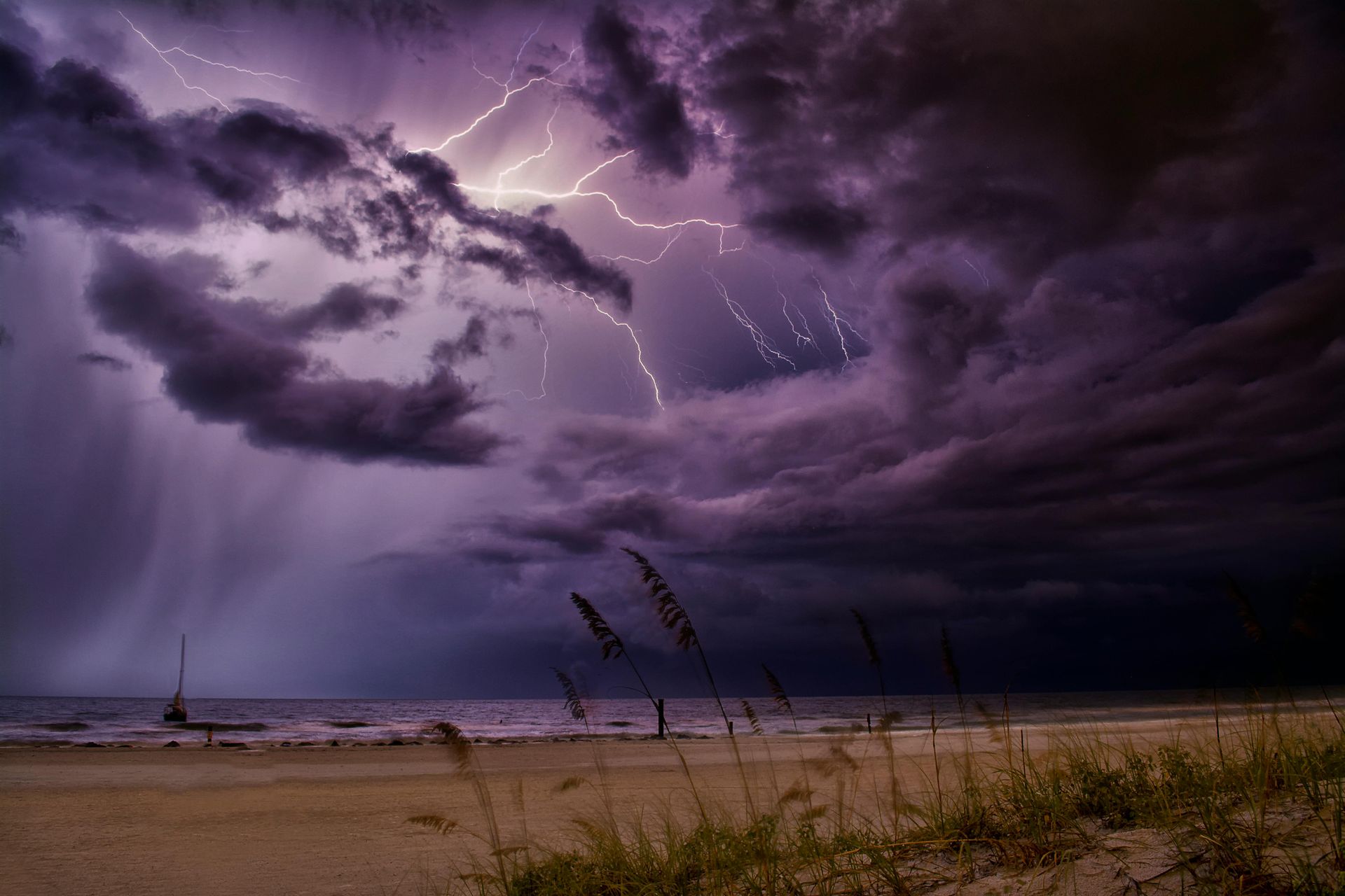 A lightning storm over a beach with purple clouds and lightning.