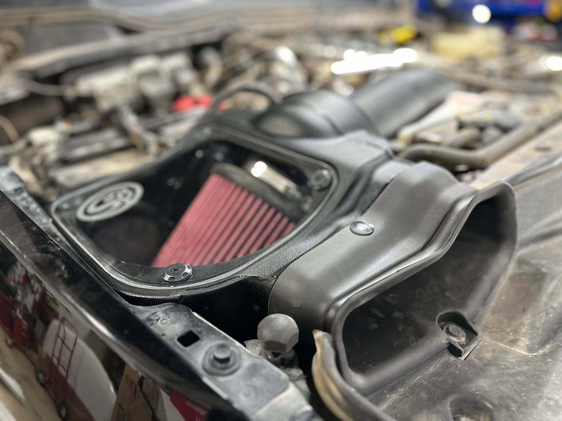 Black engine bay with a red air filter in a black box, with a tube connected.