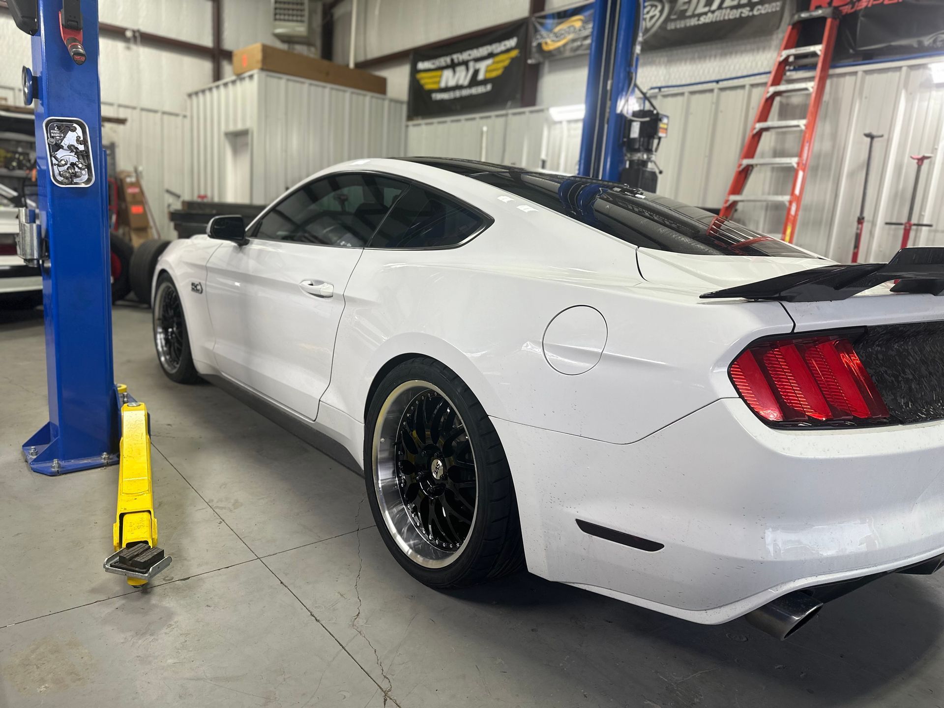 White Ford Mustang in a garage, black wheels, tinted windows.