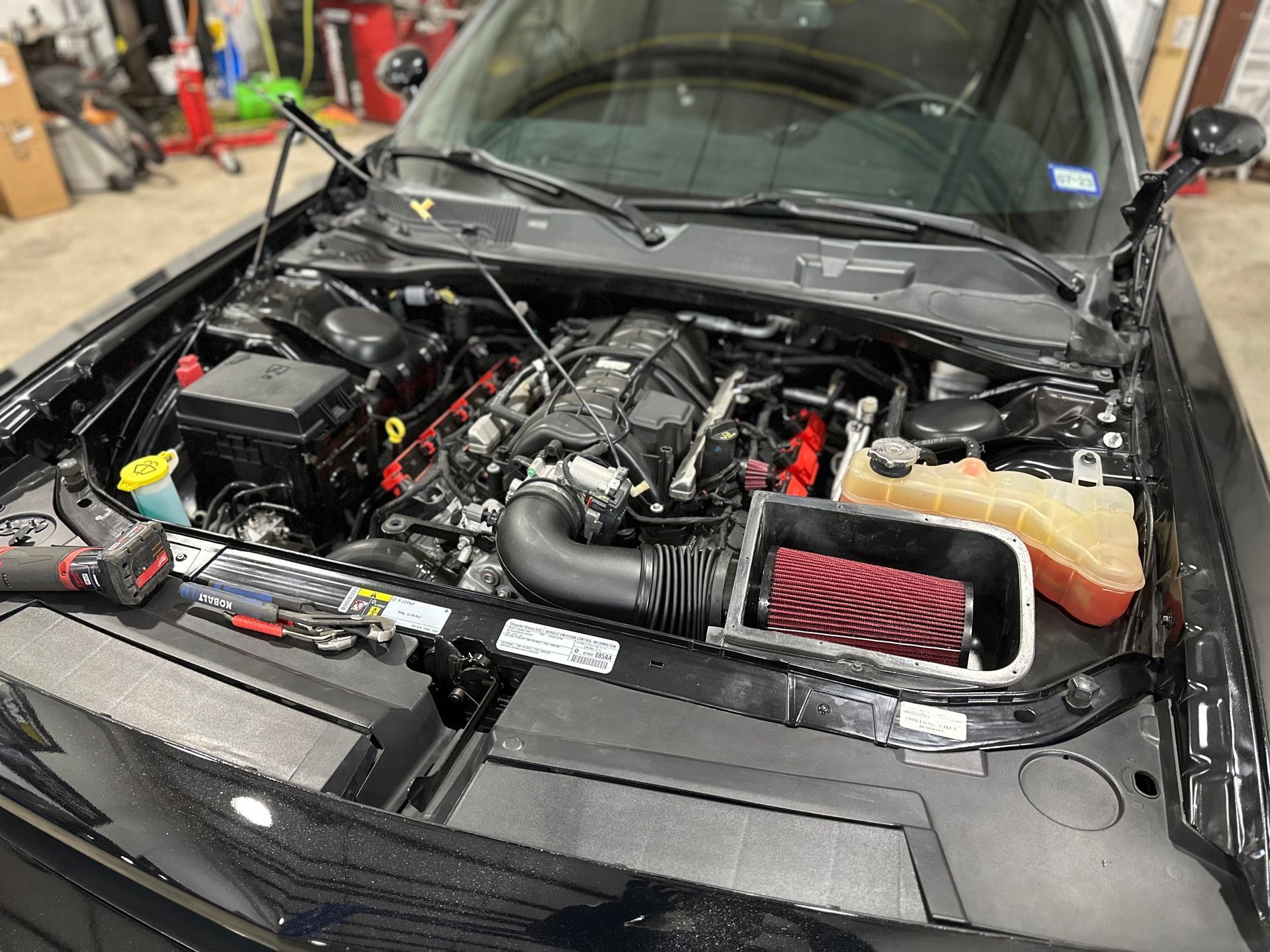 Black car engine with open hood, red air filter, and various mechanical parts.
