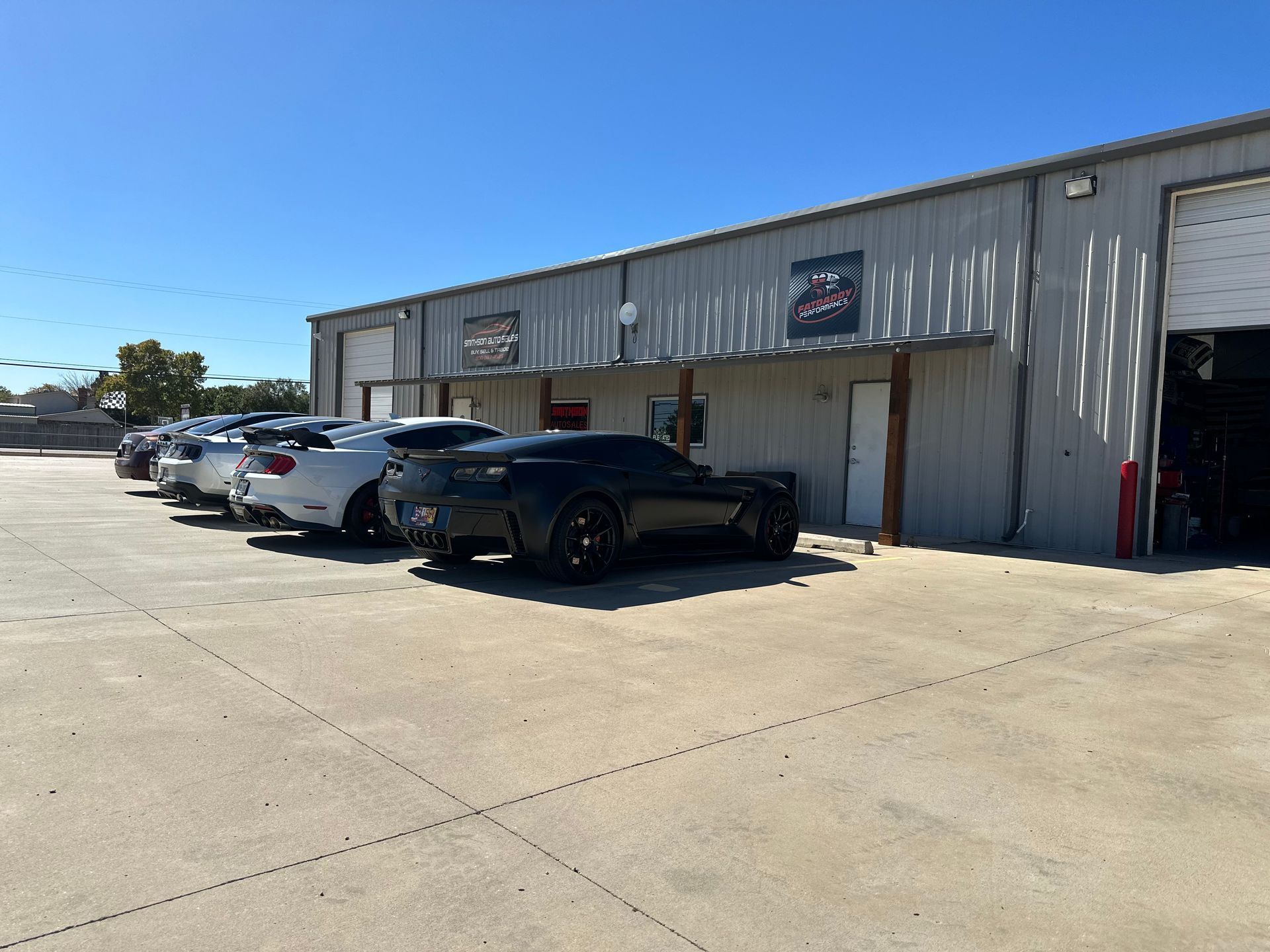 Cars parked outside a gray building with roll-up doors, sunny day.