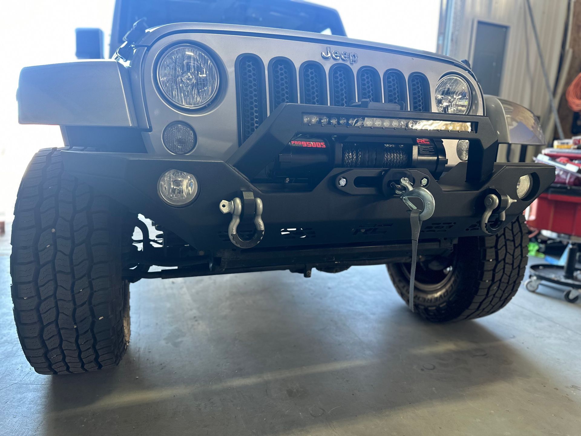Gray Jeep Wrangler with a black off-road bumper, winch, and LED light bar, parked indoors.