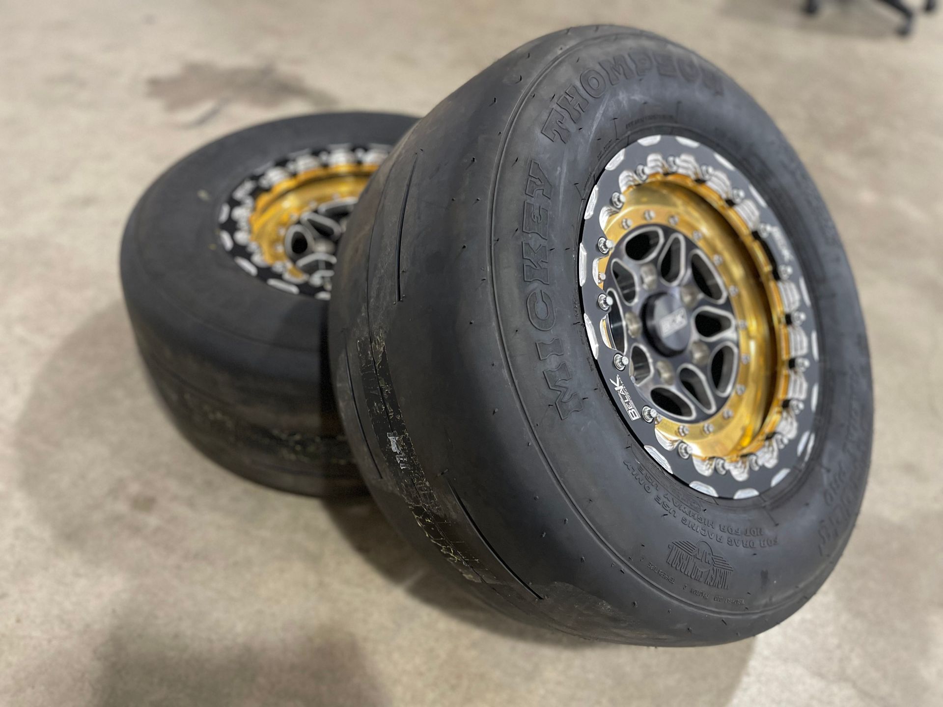 Two worn drag racing tires with gold rims.