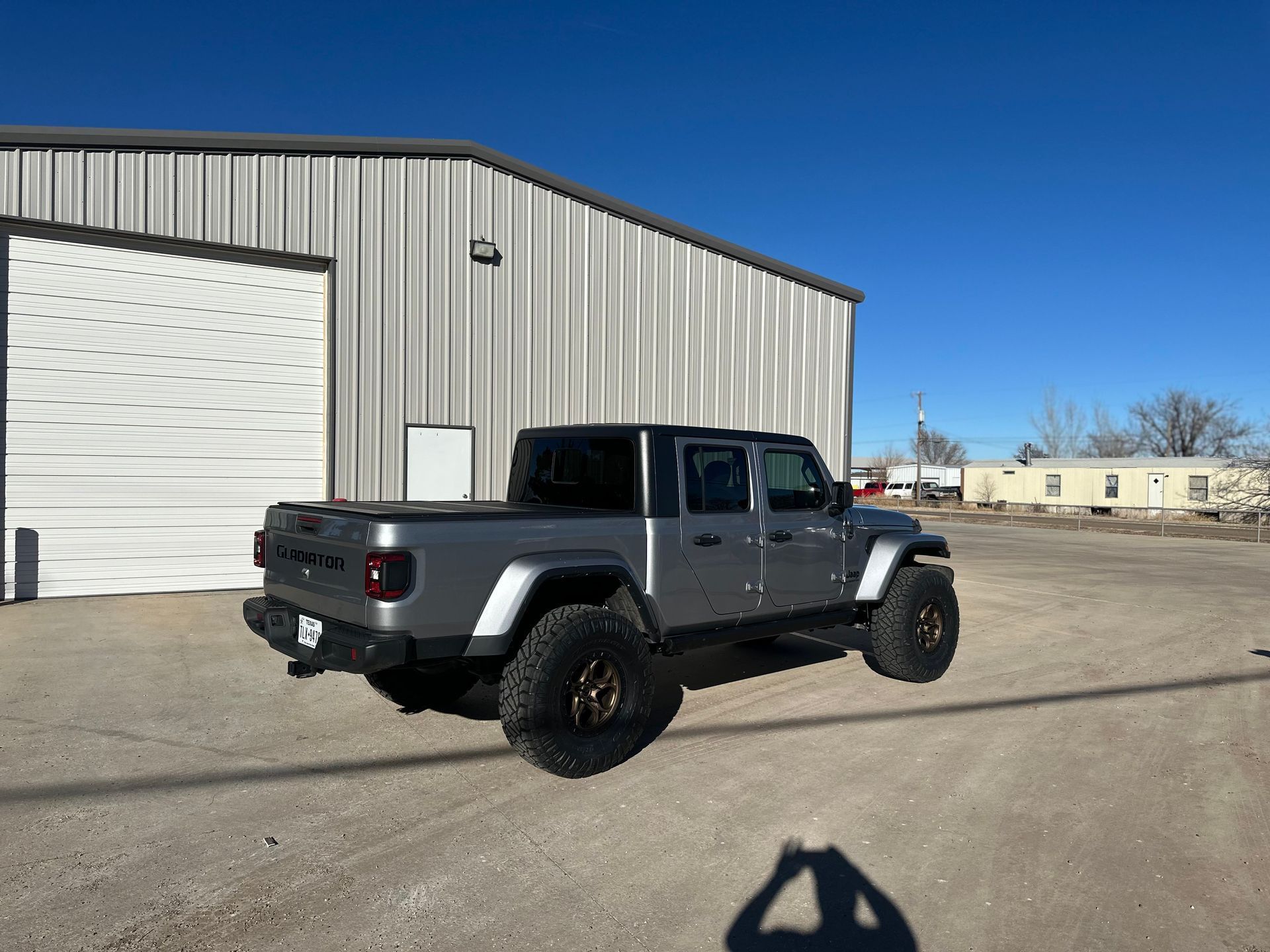 Gray Jeep Gladiator truck parked in front of a building on a sunny day.