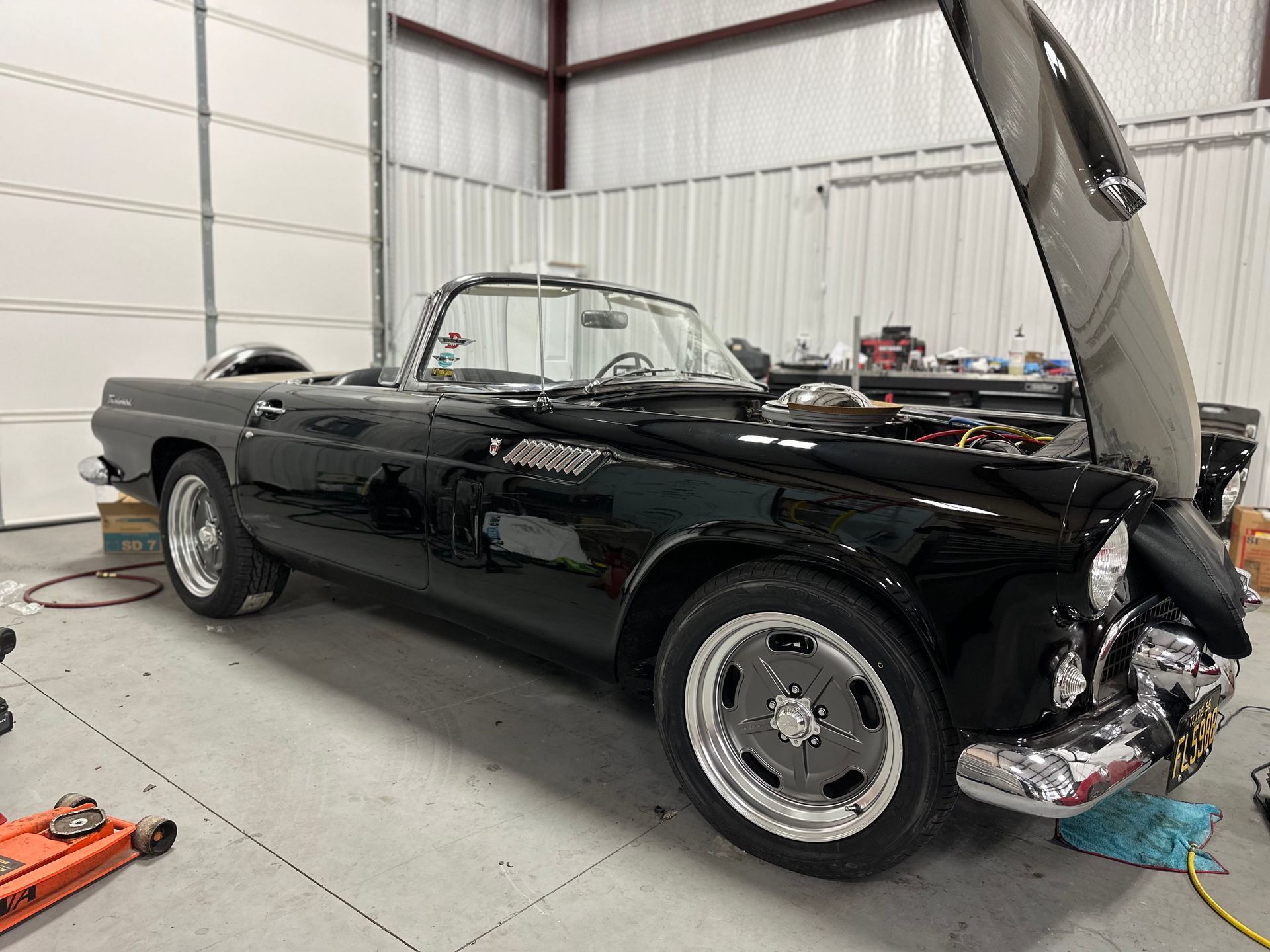Black vintage convertible car with hood up, in a garage.