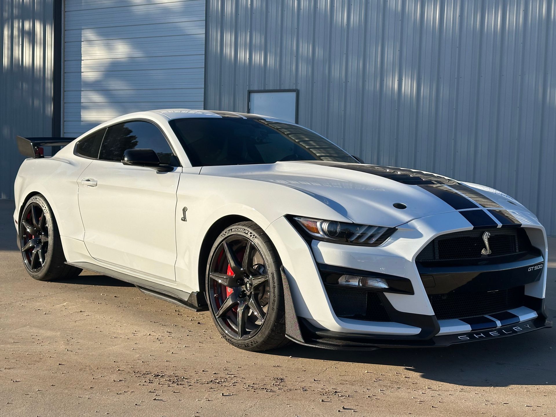 White Shelby GT500 sports car with black racing stripes parked outside a building.