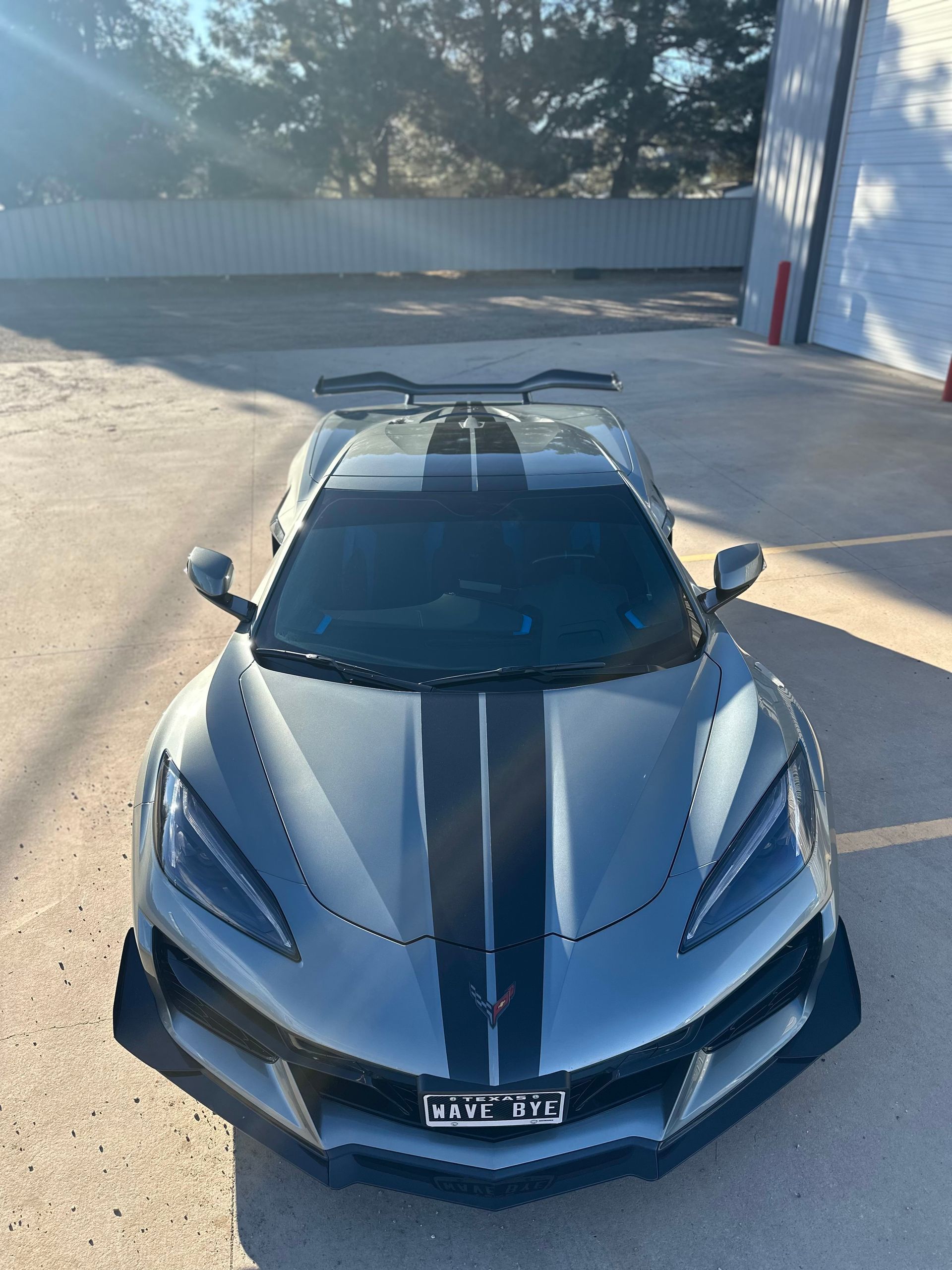 Silver sports car with black racing stripes parked outdoors.