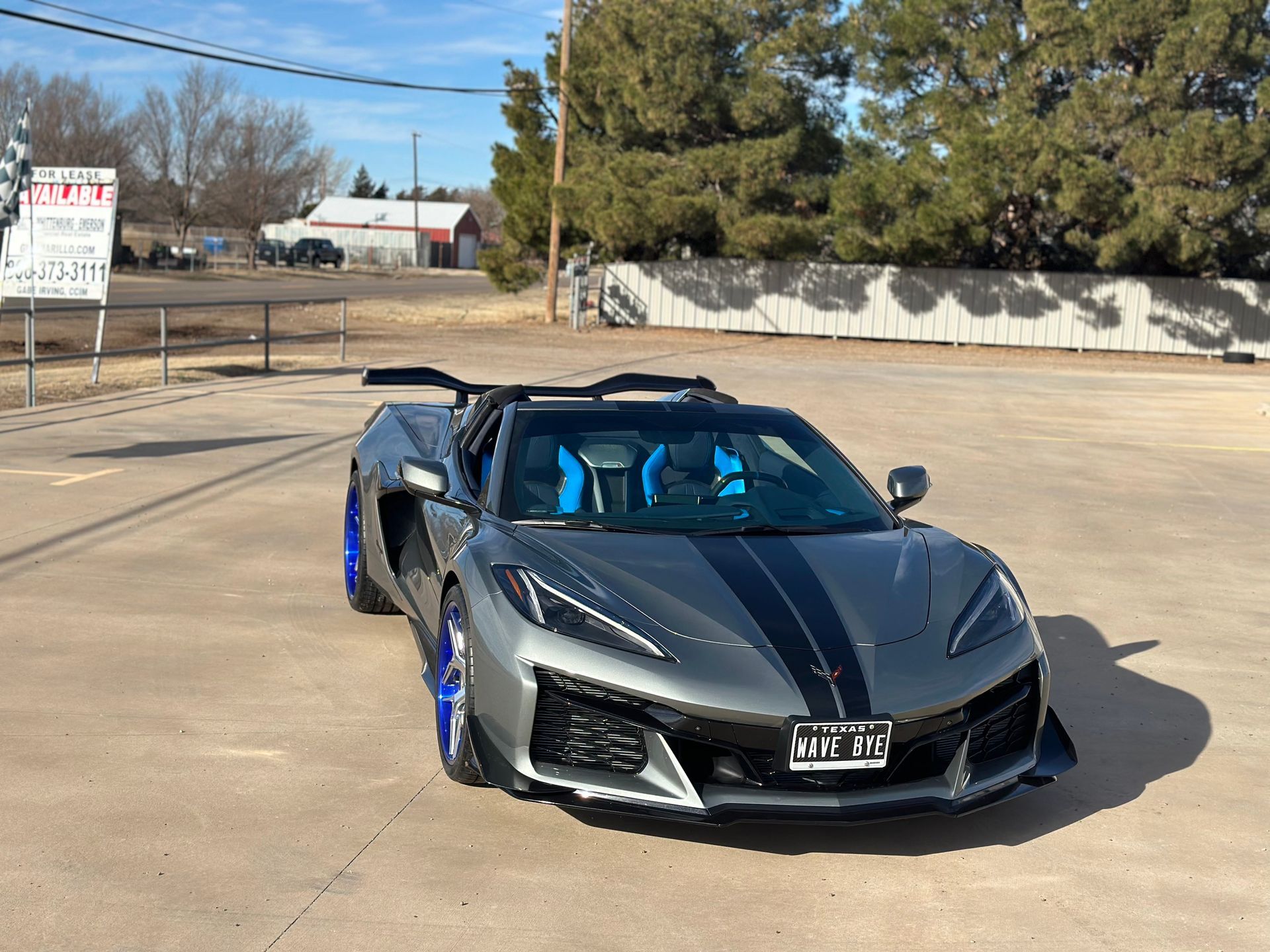 Gray Corvette sports car with blue accents and black stripes parked outside on a sunny day.