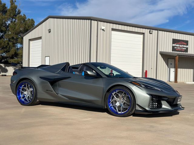 Gray convertible sports car with blue accents, parked in front of a metal building.
