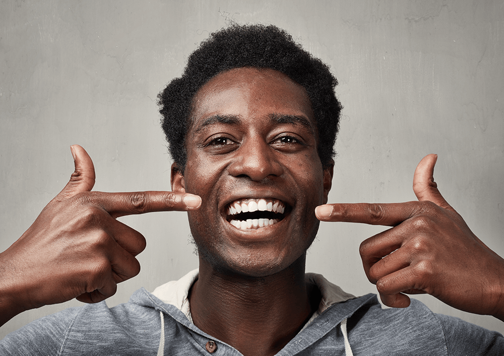 A man is pointing at his teeth and smiling.