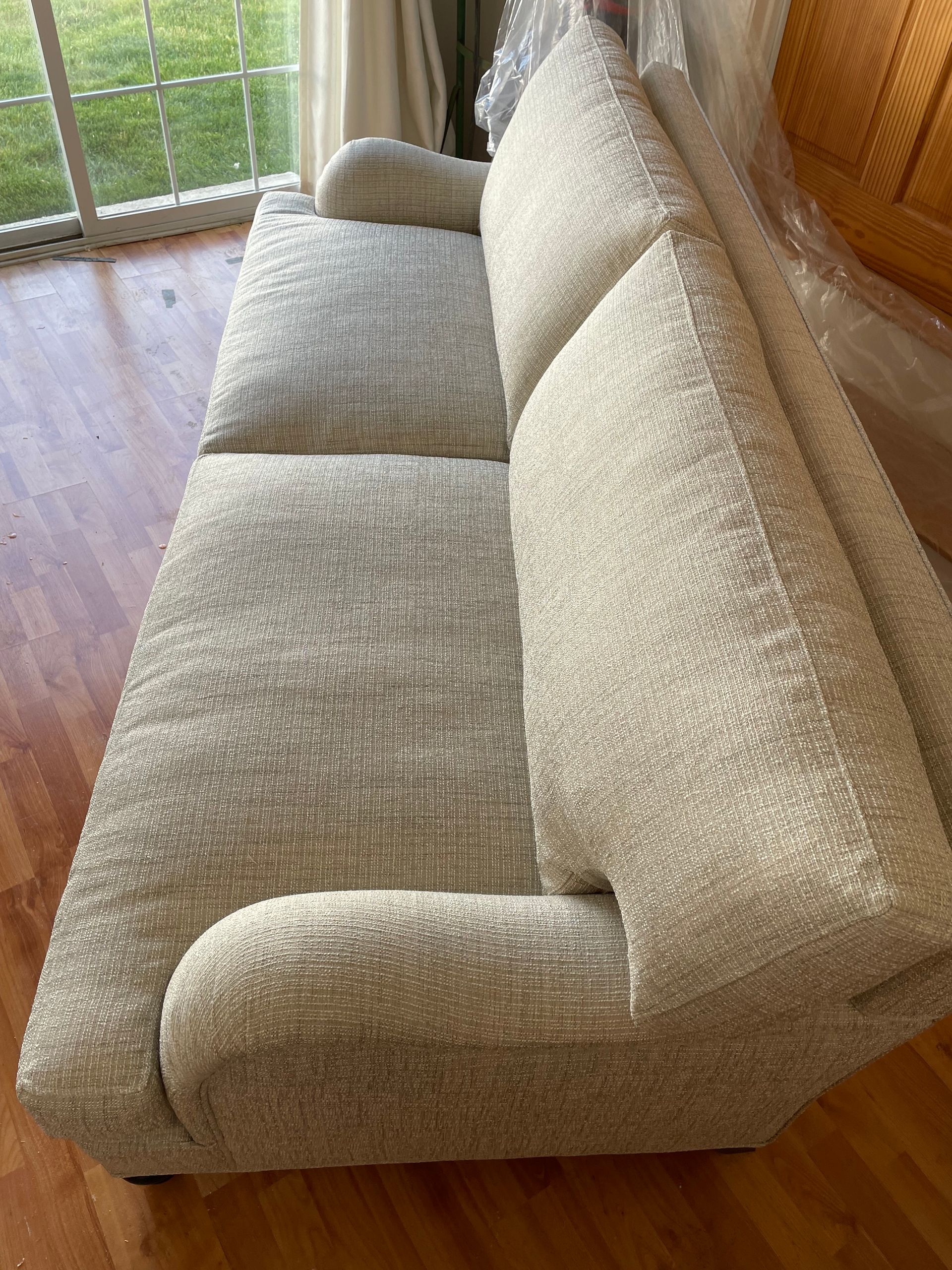 A white couch is sitting on a wooden floor in a living room next to a window.