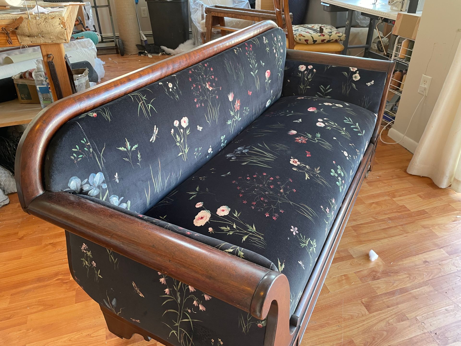 A black couch with flowers on it is sitting on a wooden floor.
