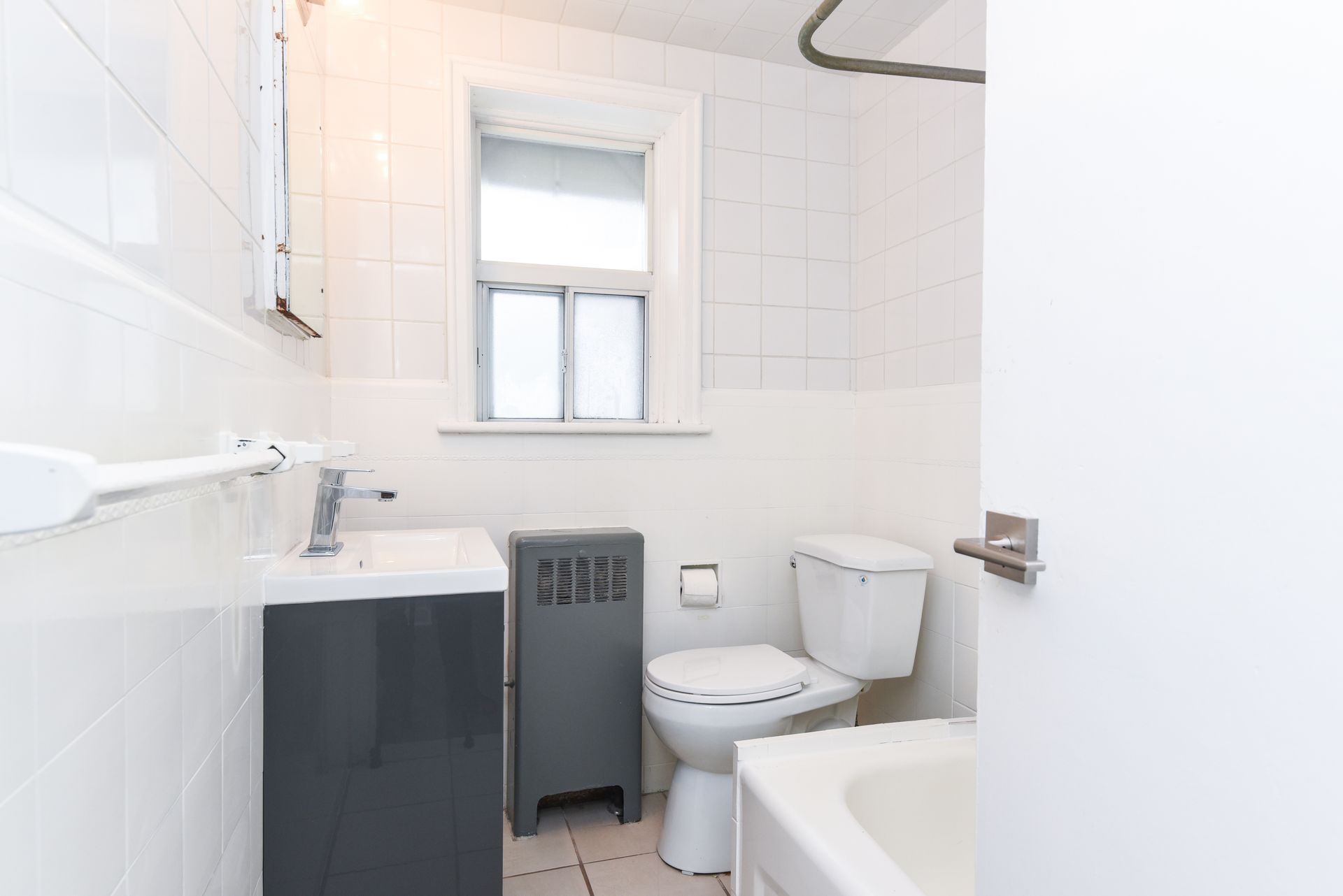 Small white bathroom with toilet, sink, bathtub, window, and black radiator cover