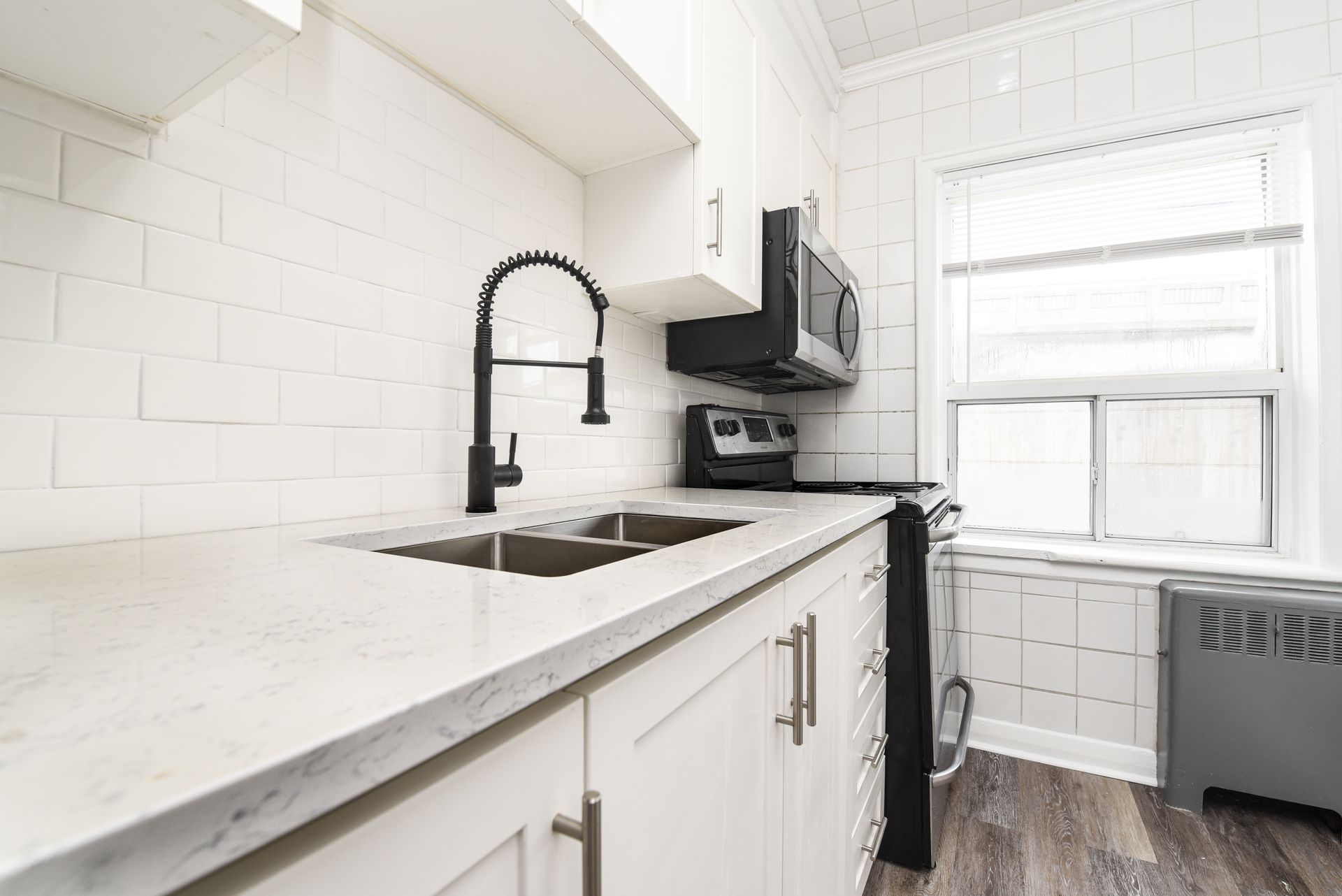 Bright white kitchen with black faucet, marble countertop, stove, and window over the sink