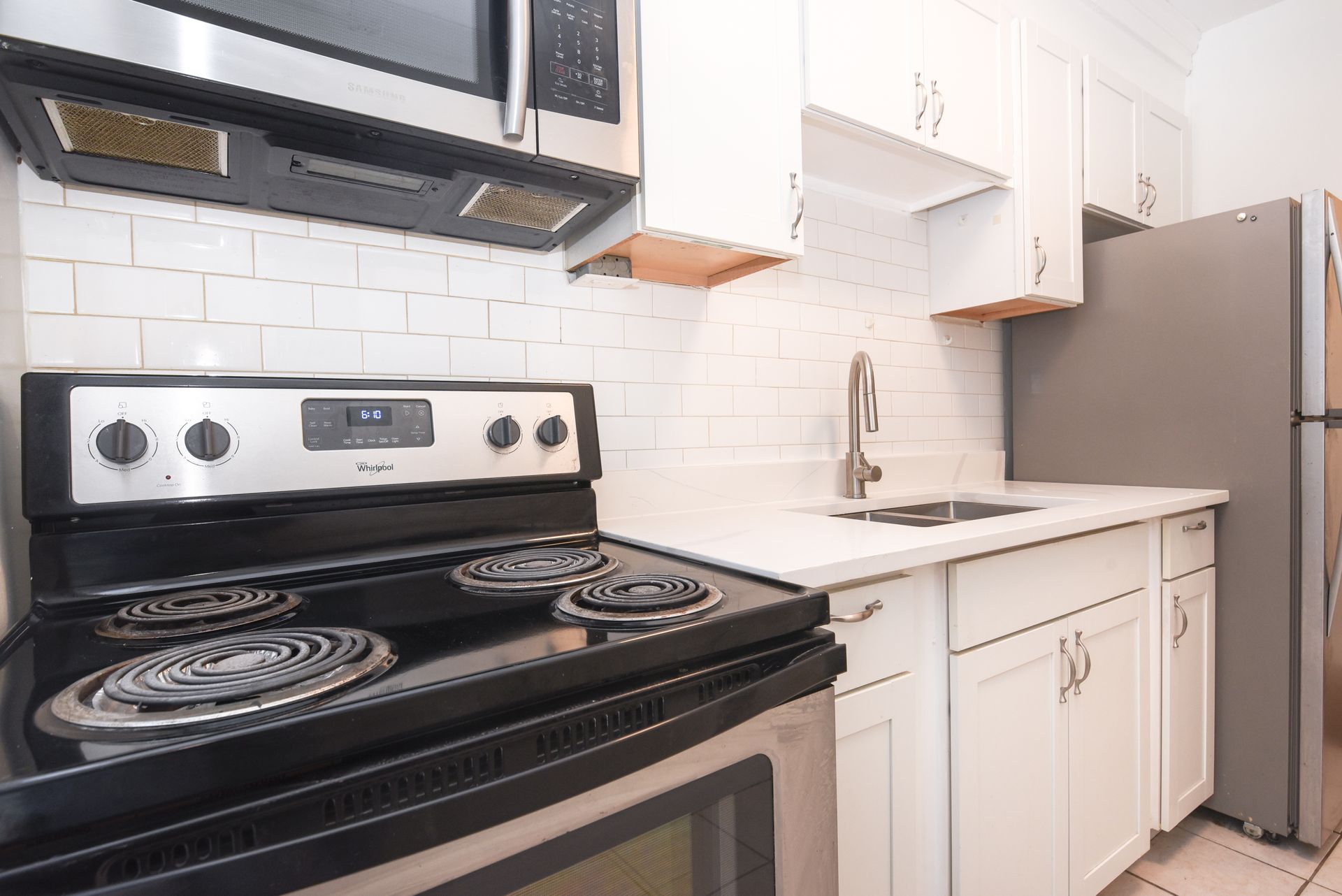 Bright white kitchen with black stove, stainless microwave, sink, cabinets, and refrigerator.