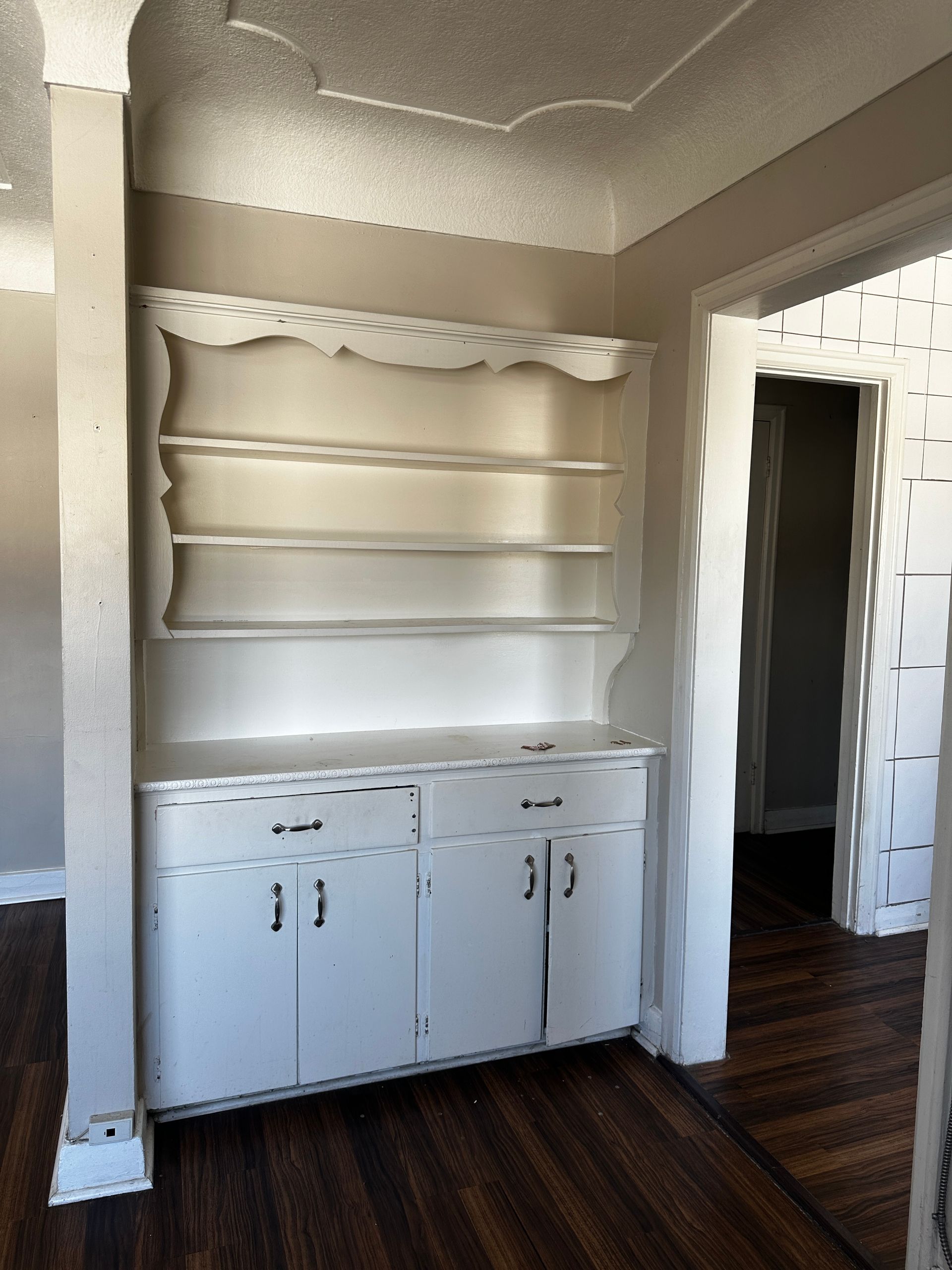 Built-in white cabinet and shelves against a beige wall in a room with dark wood floors