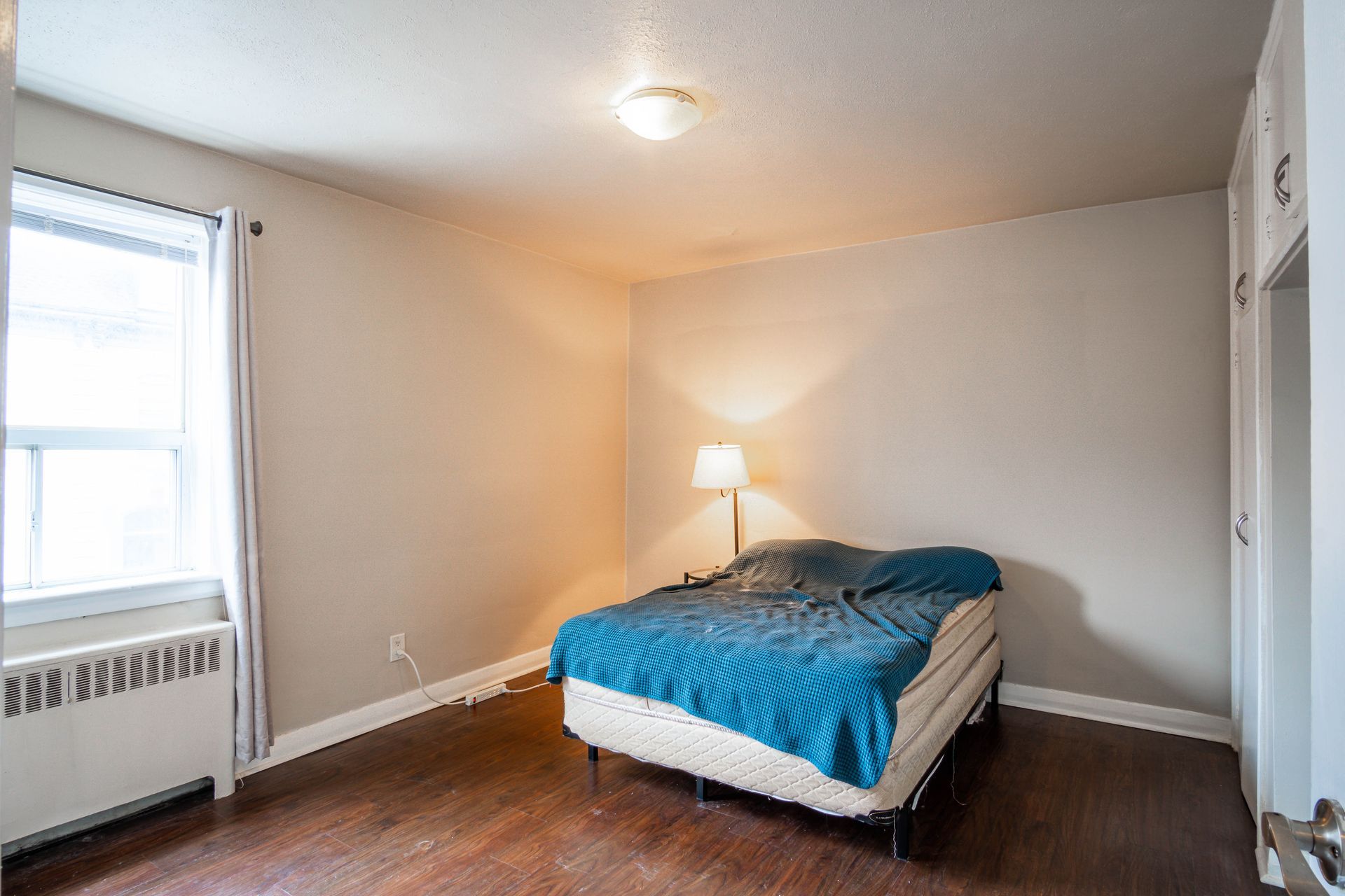 Simple bedroom with a bed, blue comforter, lamp, and window air conditioner