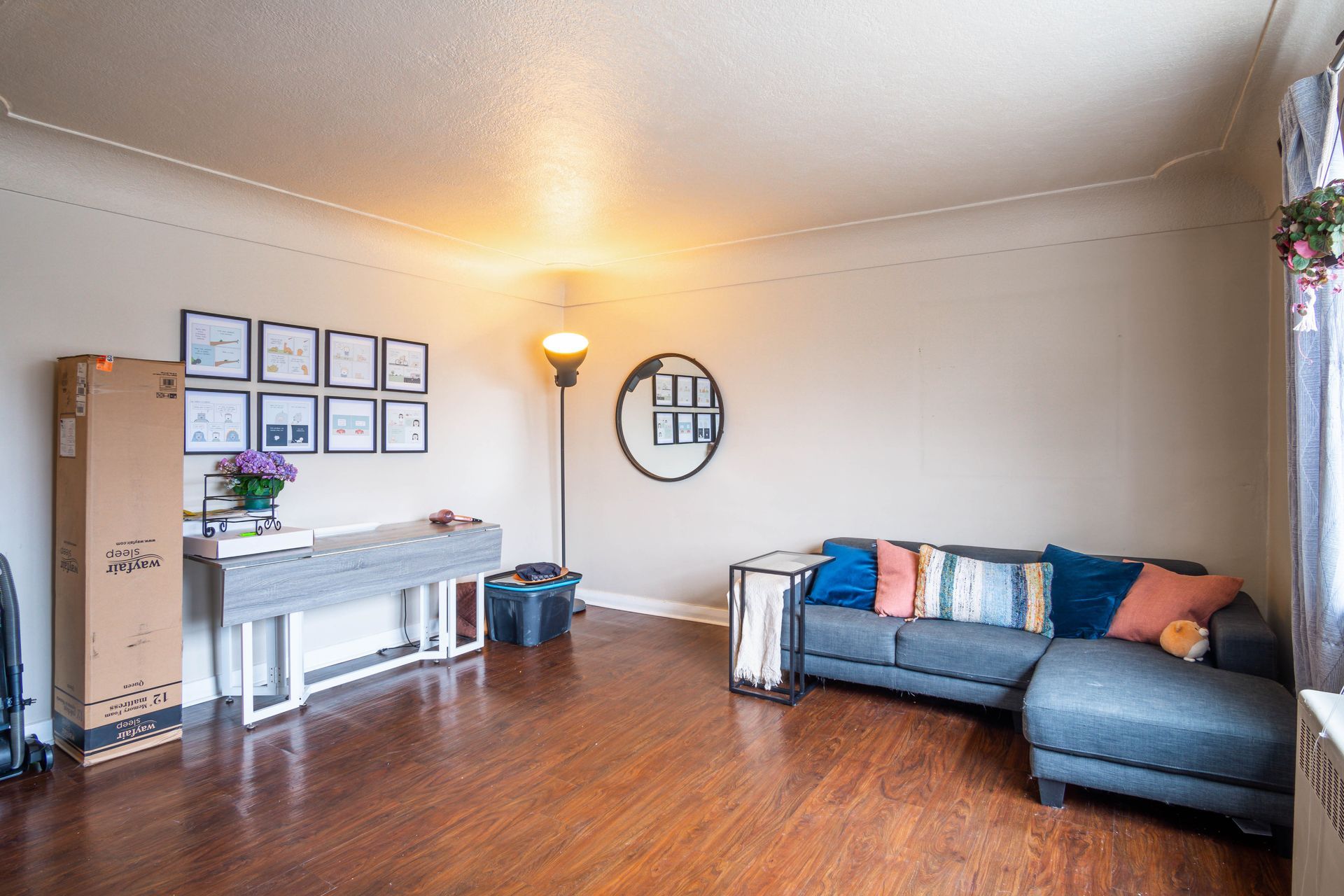 Cozy living room with gray sofa, piano, framed wall art, wood floors, and warm lamp lighting