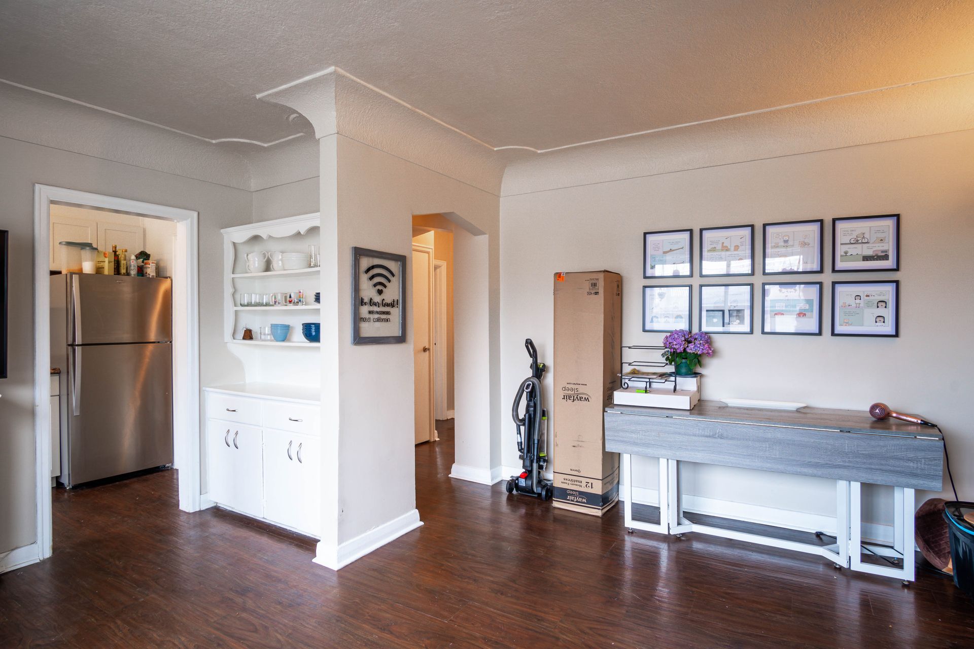 Open kitchen and living area with stainless fridge, dark wood floors, wall art, and console table.