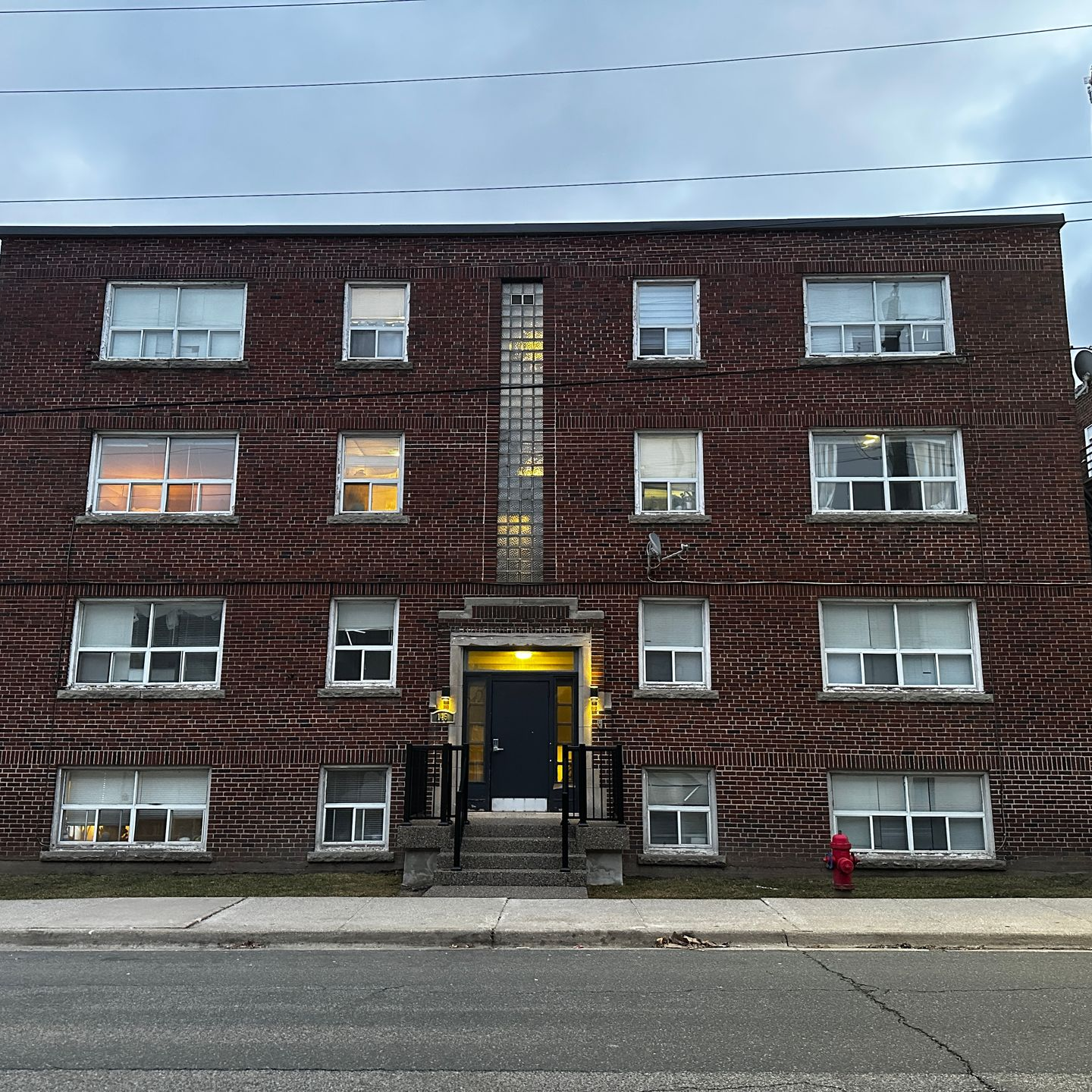 Three-story brick apartment building with lit entrance and windows at dusk