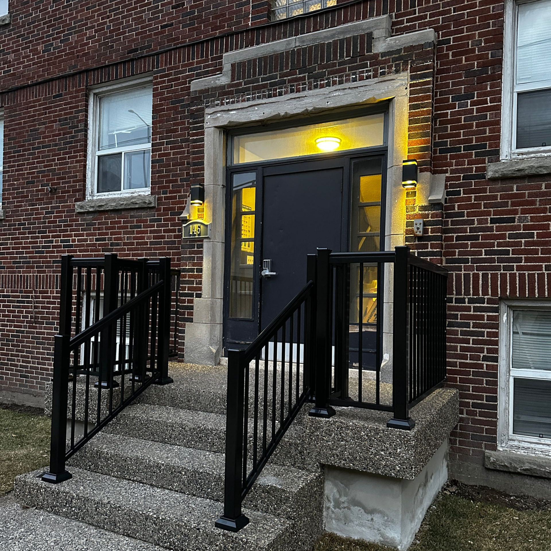 Brick apartment entrance with black railings and lit doorway at dusk