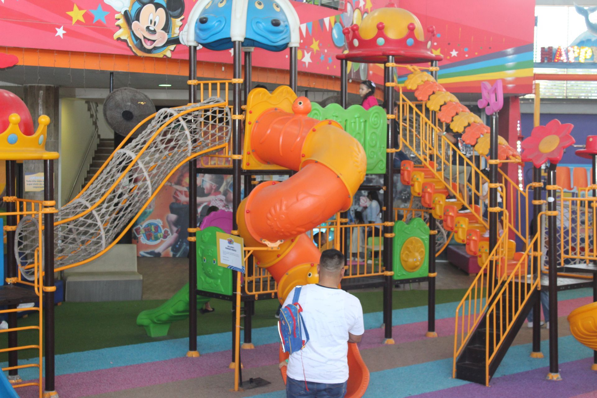Colorful indoor playground with slides, climbing stairs, and a child standing in front