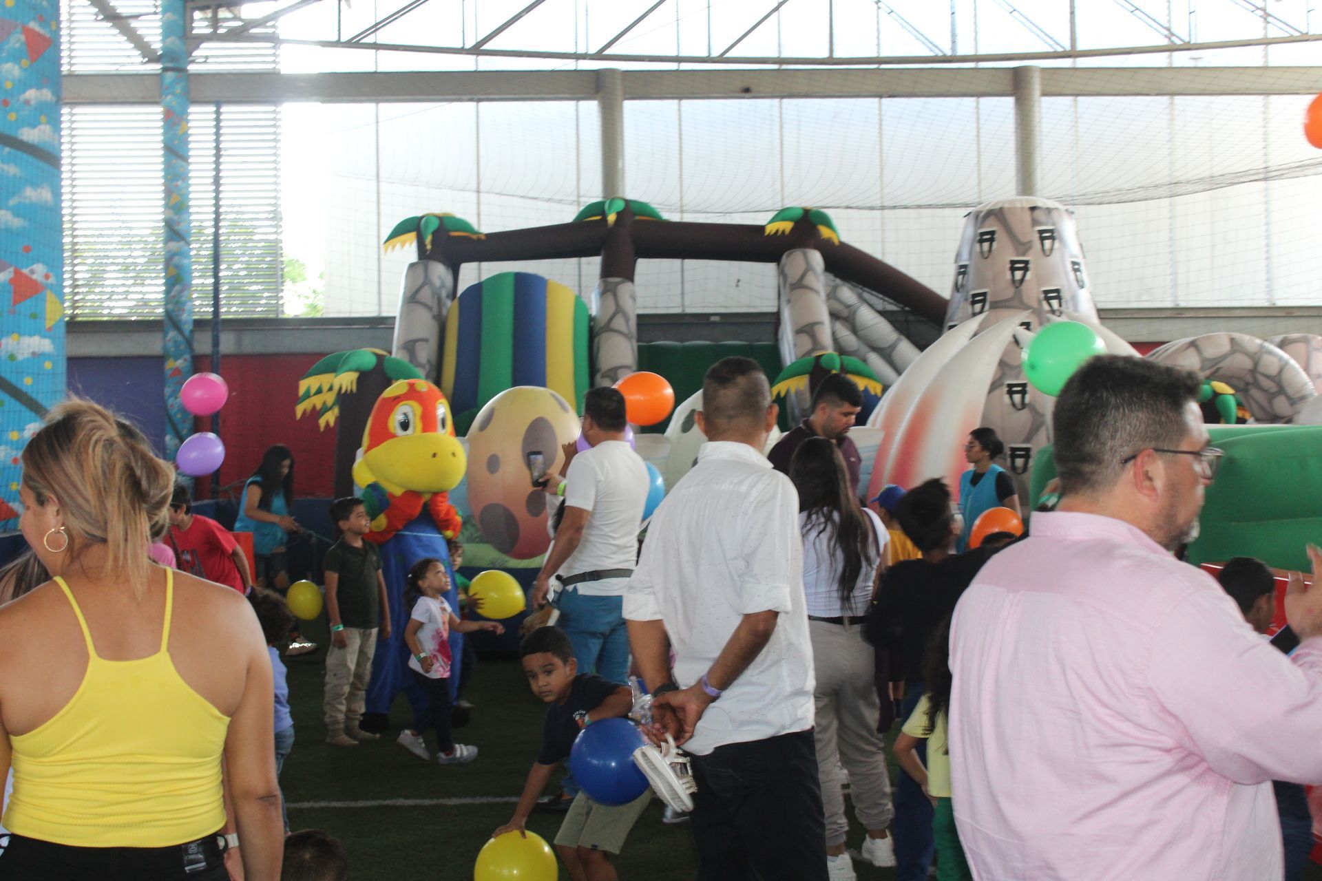 People at an indoor inflatable bounce park with colorful balloons and play structures
