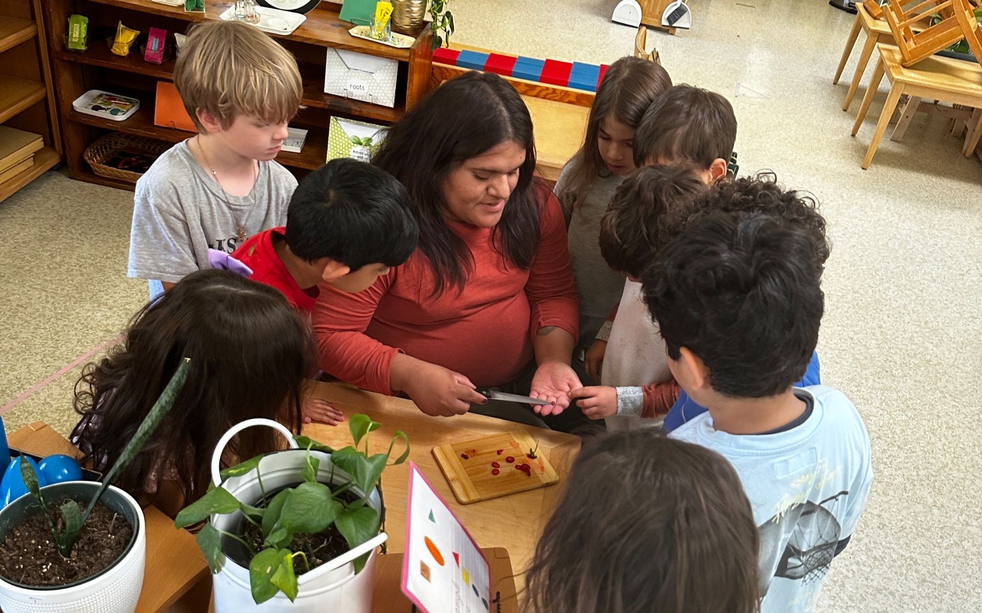 Children gathered around a table with a Montessori guide, working together on a classroom craft activity.