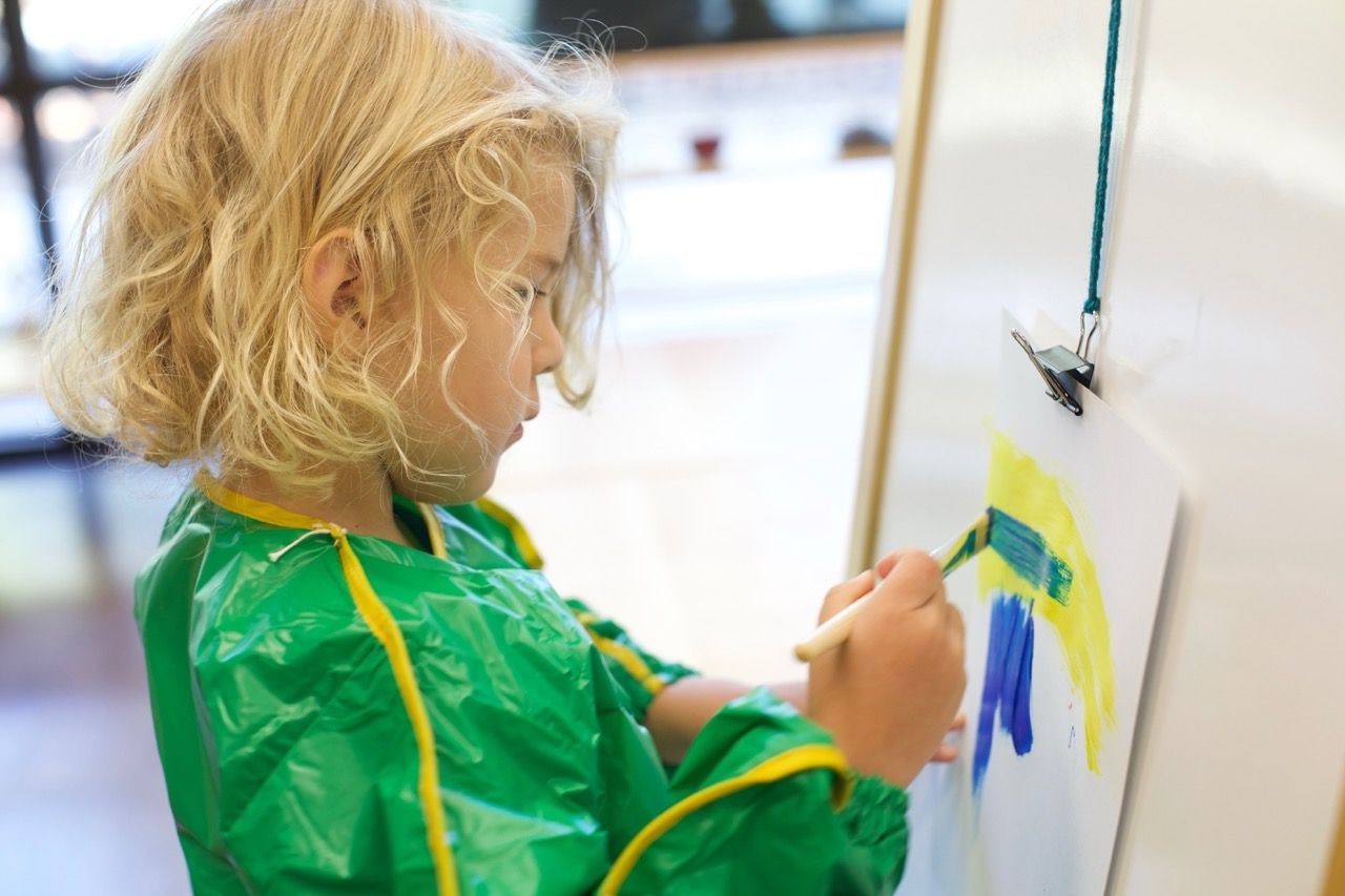 Child in a green smock painting on a canvas with a paintbrush