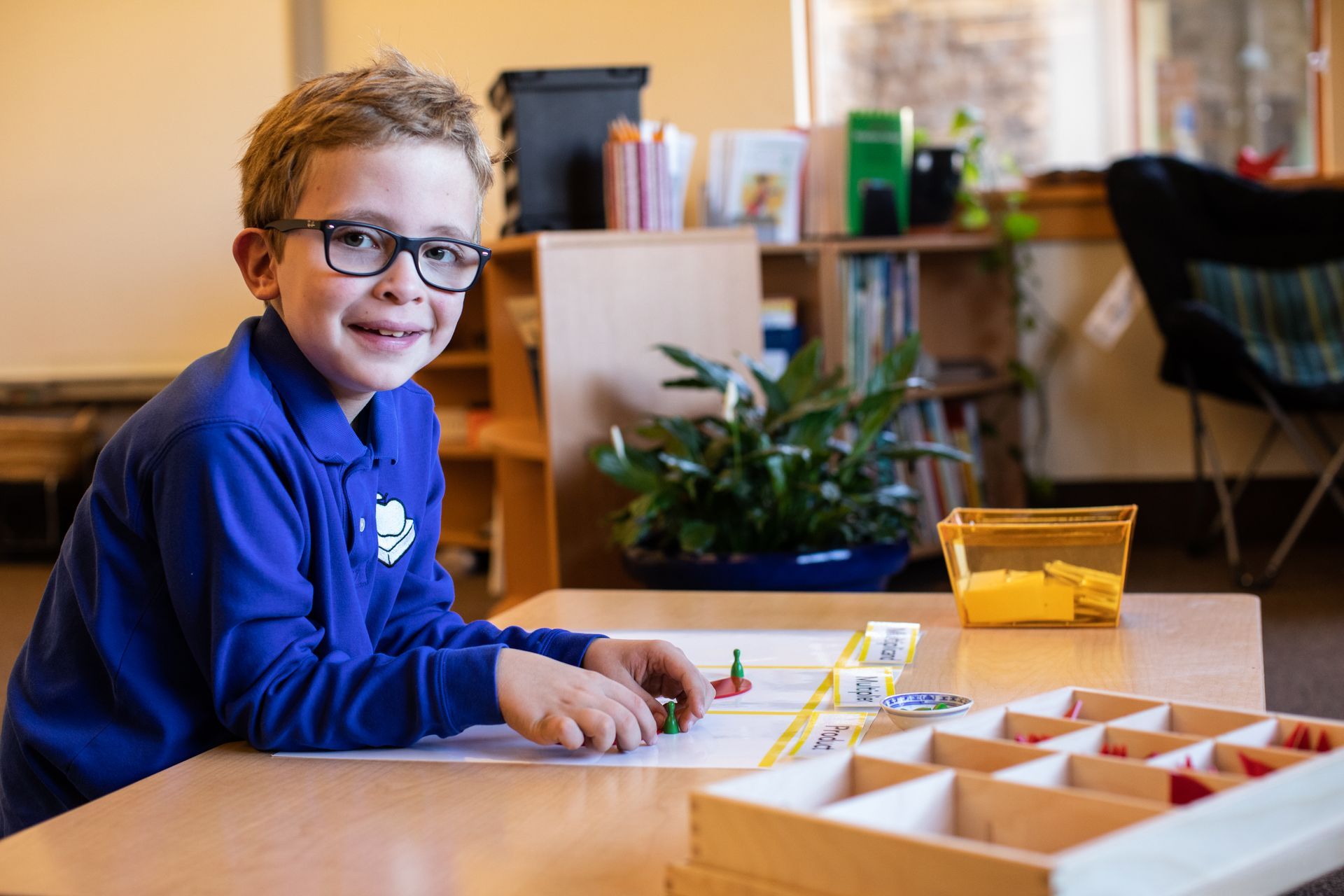 Child in blue shirt and glasses playing with blocks at a classroom table