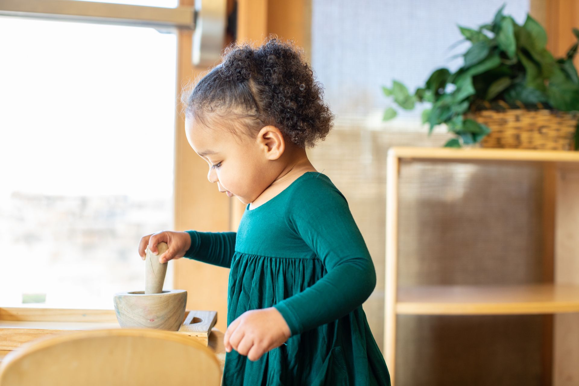 Child stirring a bowl at a wooden table by a sunlit window