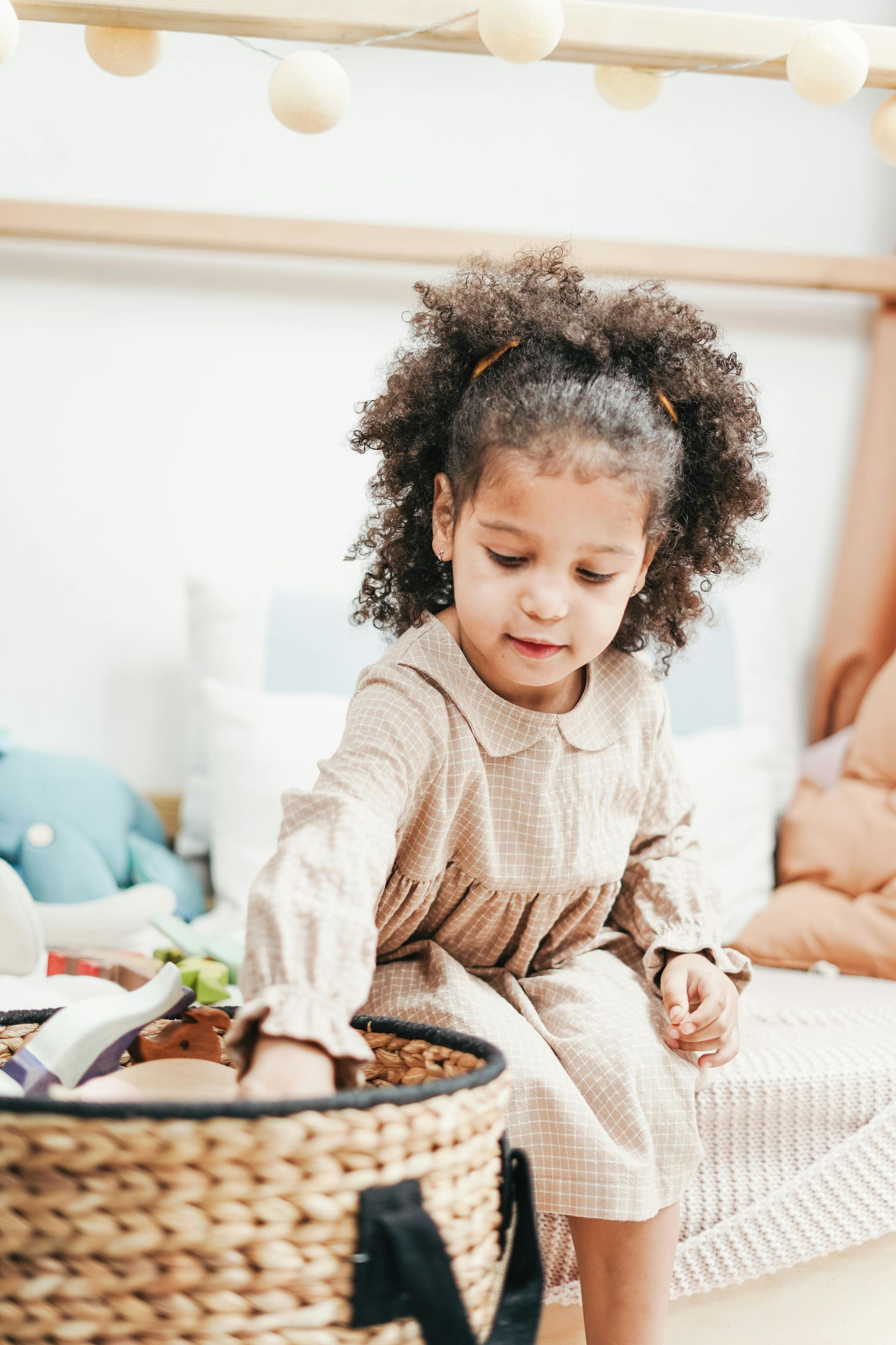Toddler in beige sweater reaching into a woven basket in a bright playroom