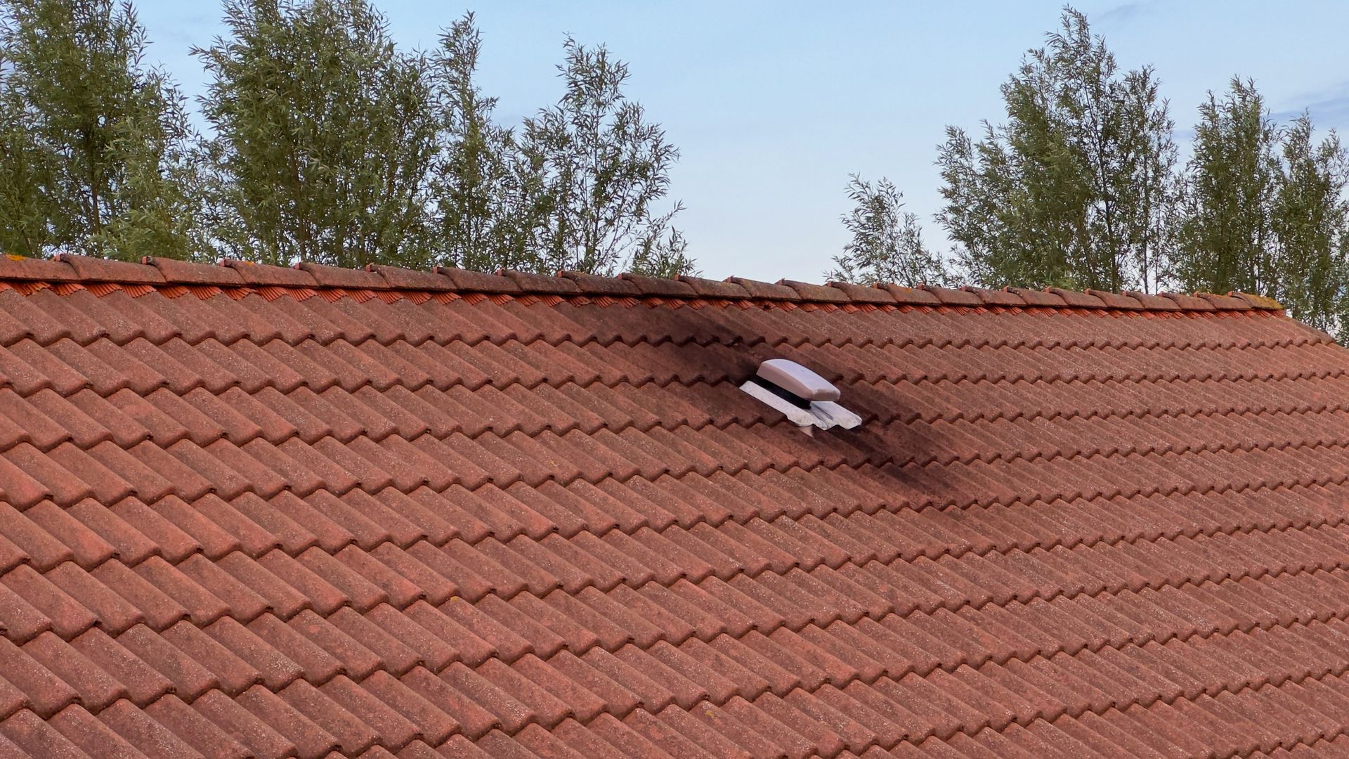 Red tile roof with a dark, charred area and debris. Trees and blue sky in the background.