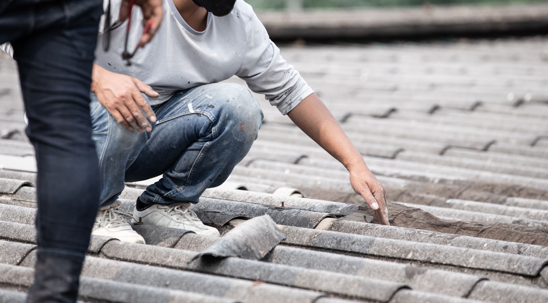 Person examining a tiled roof, assessing damage. Outdoors, daylight.