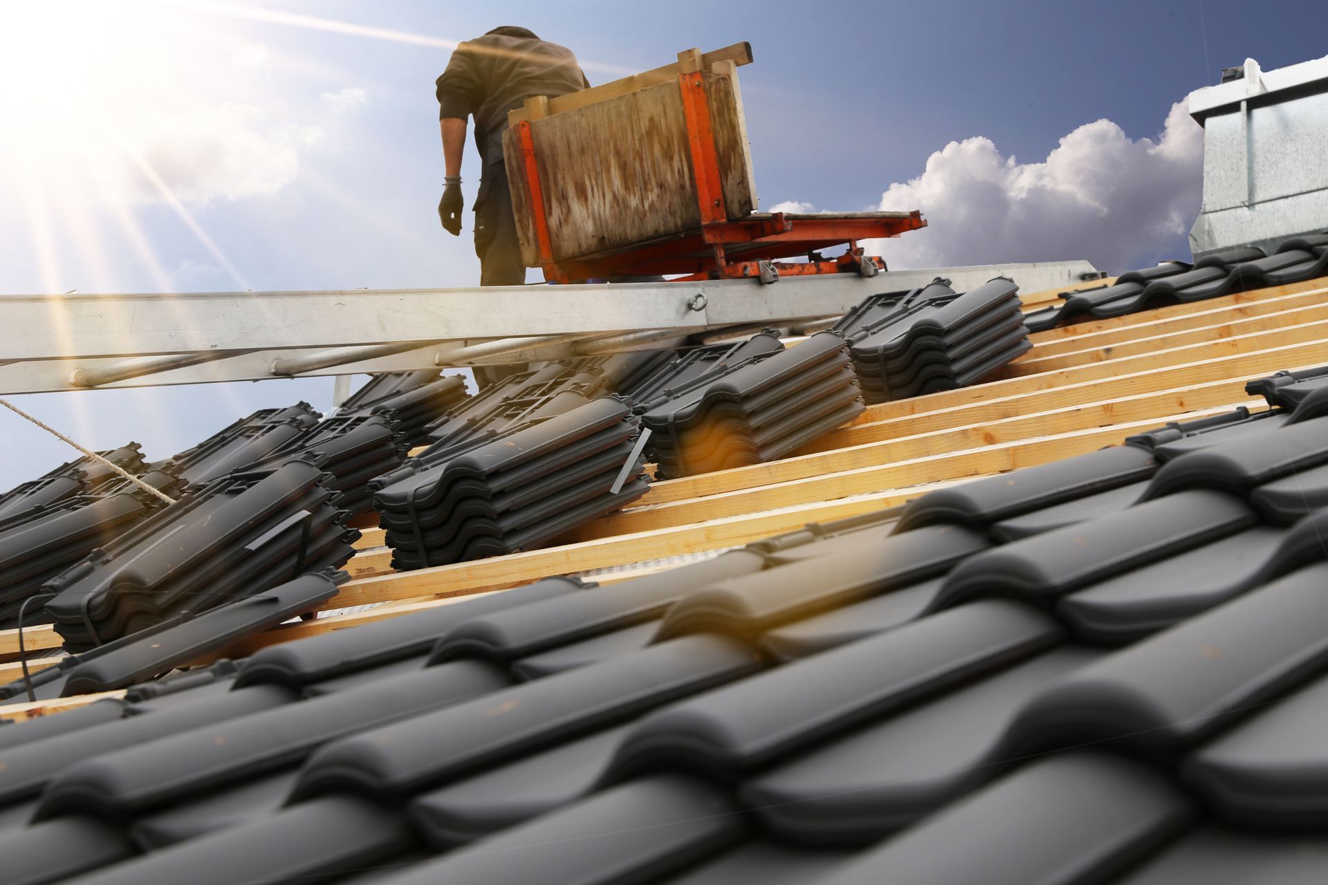 Roofer installing dark gray roof tiles on a sunny day.