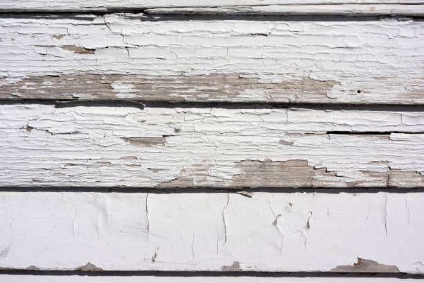White painted wooden siding with peeling paint, showing weathered wood grain.