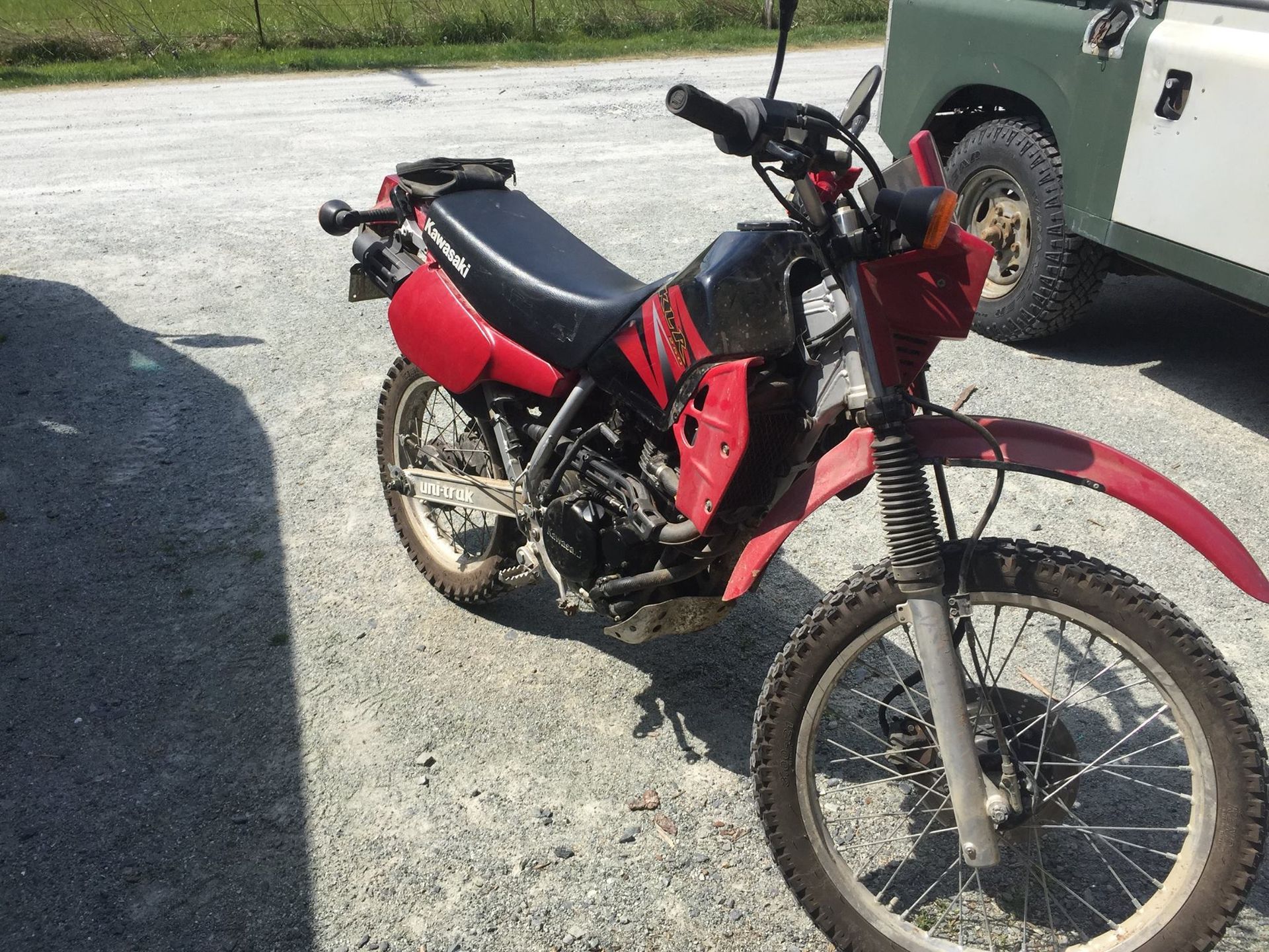 A red dirt bike is parked next to a land rover