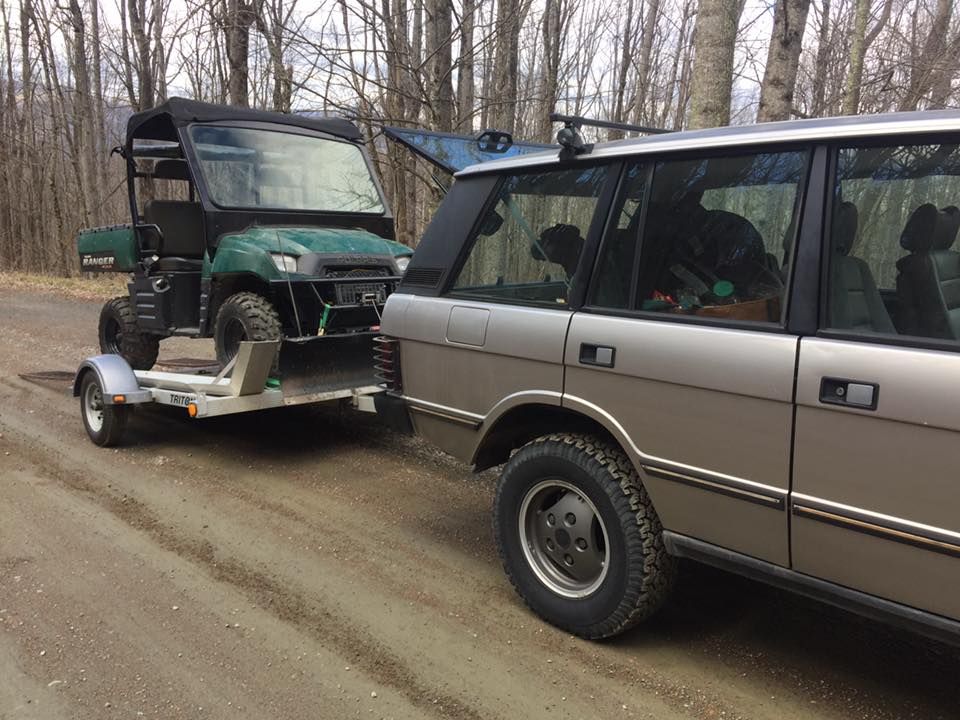 A range rover is towing a golf cart down a dirt road.
