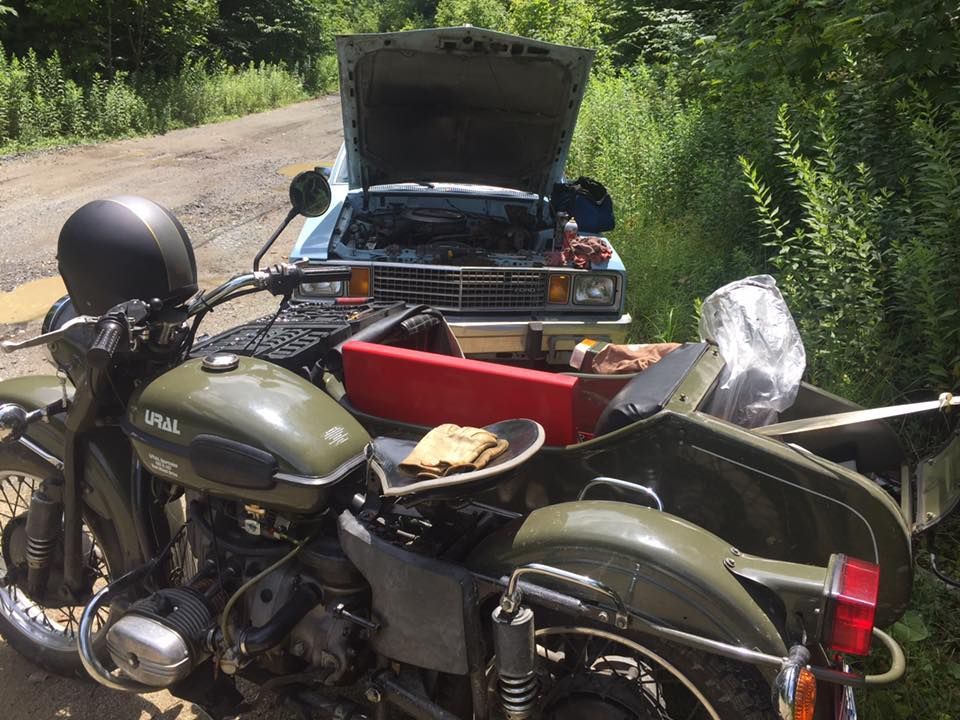A motorcycle with a sidecar is parked next to a car with the hood open.