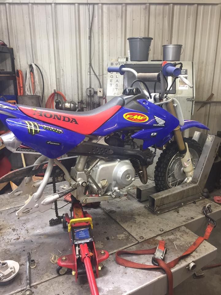 A blue and red dirt bike is sitting on a jack in a garage.