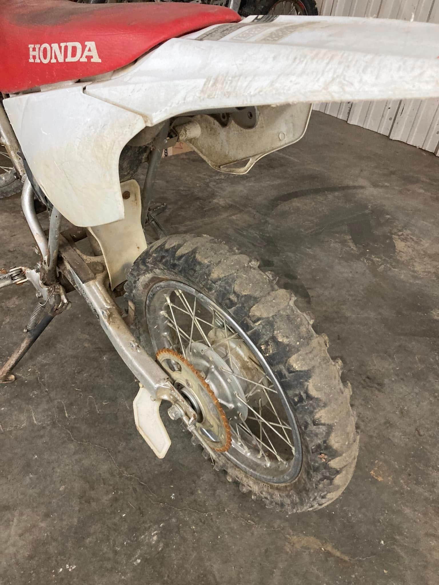The rear wheel of a honda dirt bike is covered in mud.