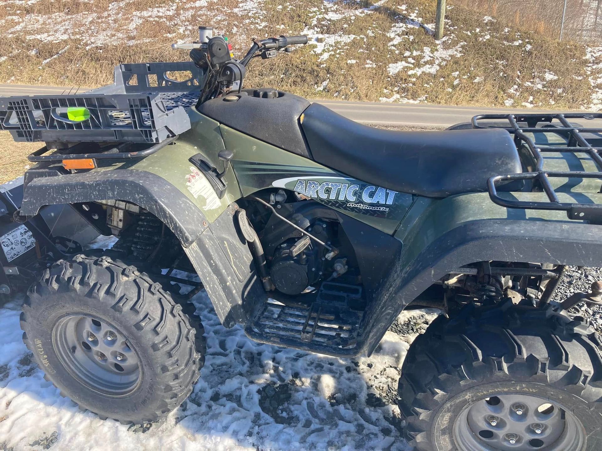 A green atv is parked in the snow on the side of the road.