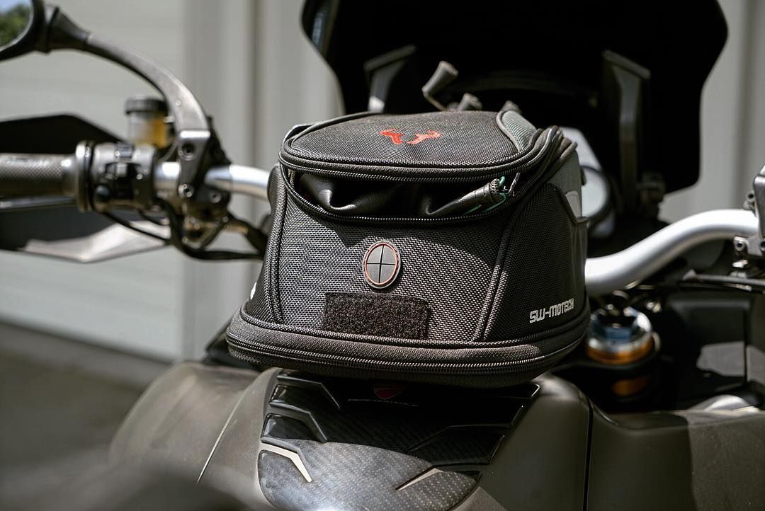 A small black bag is sitting on the handlebars of a motorcycle.