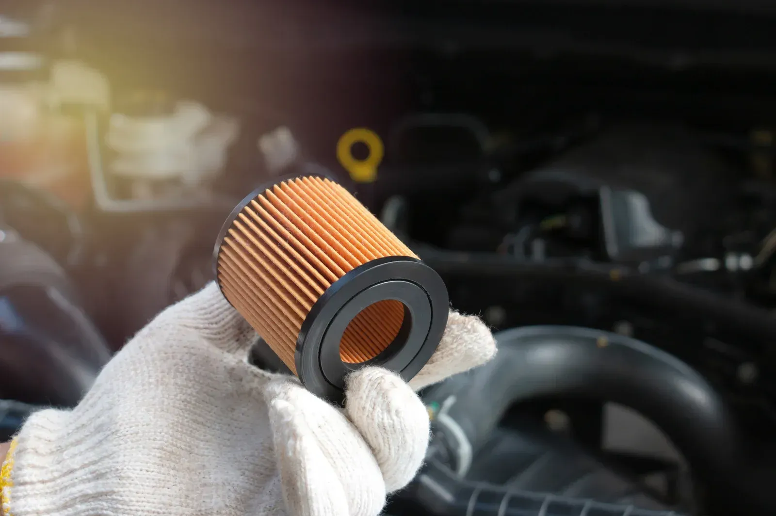 A person is holding an oil filter in front of a car engine.